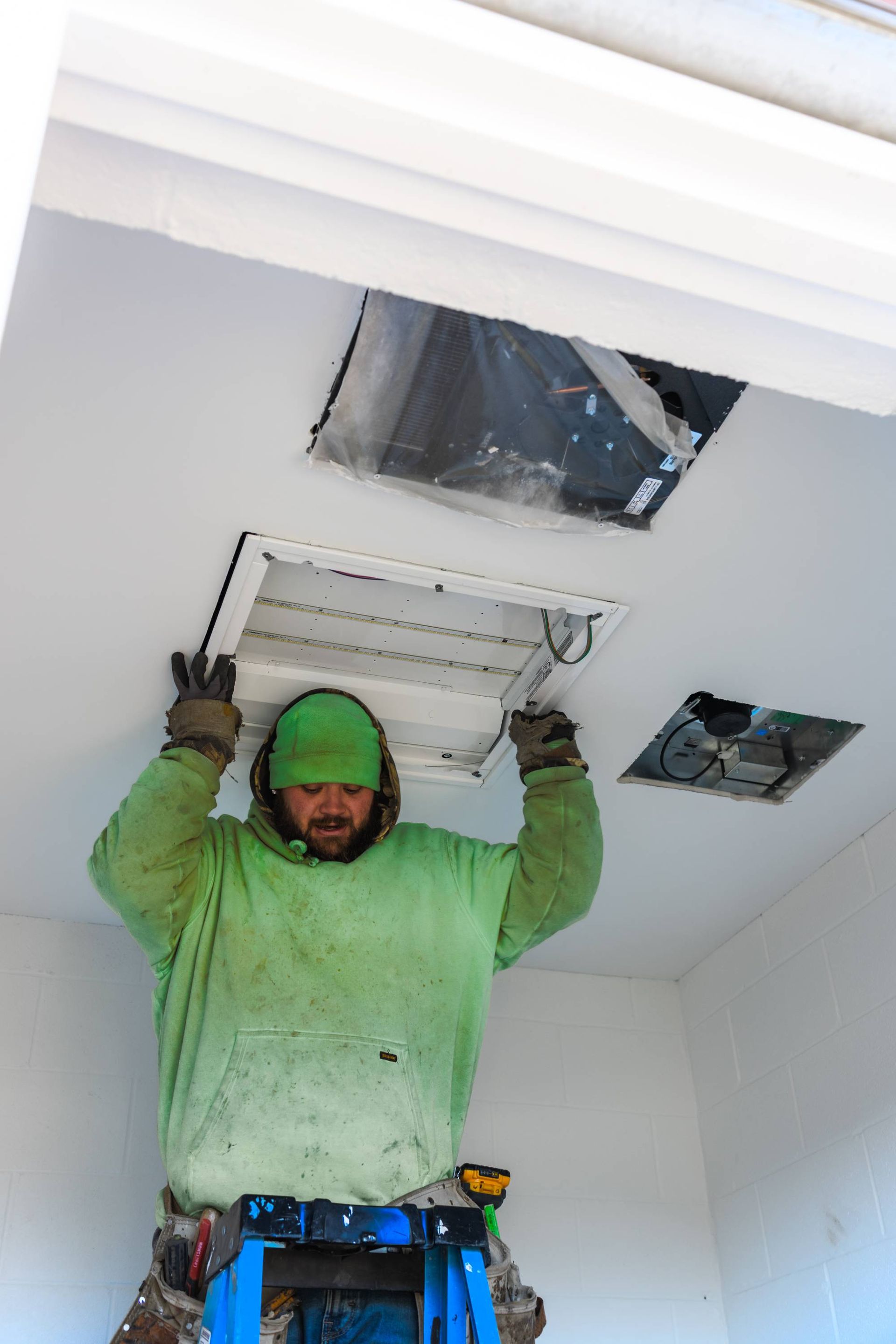 Person on ladder installing a light fixture in a white ceiling.