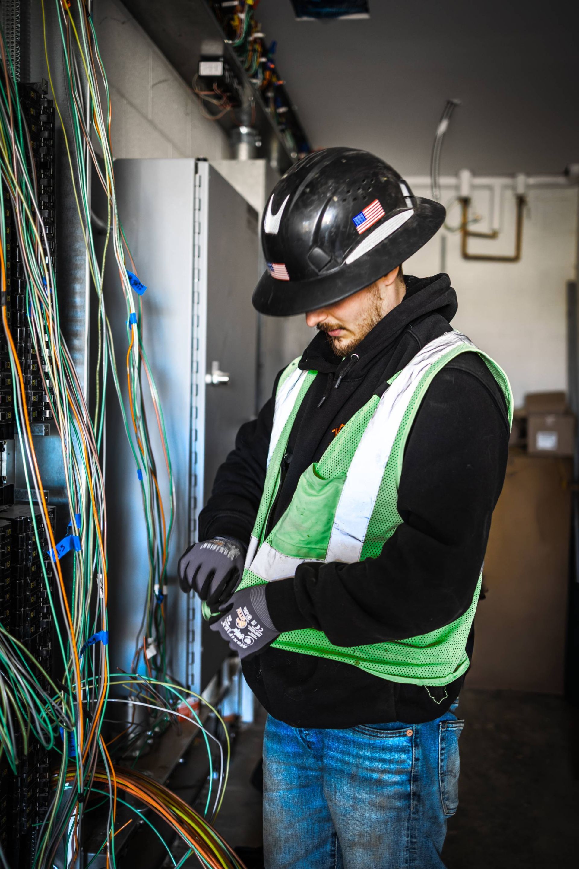 Person wearing hard hat and safety vest working with wires in an industrial setting.