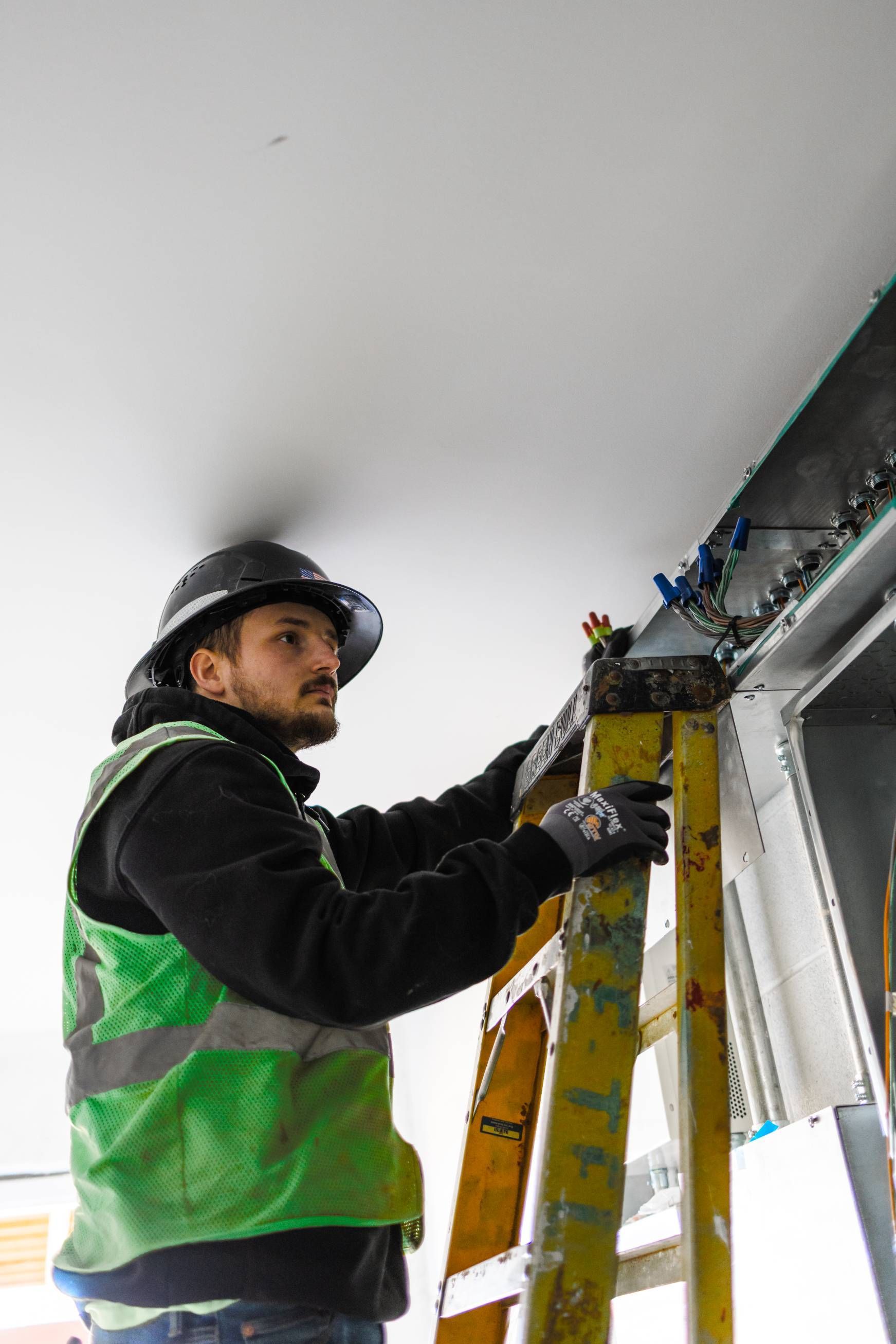 Construction worker in hard hat and safety vest on ladder, working on ceiling.