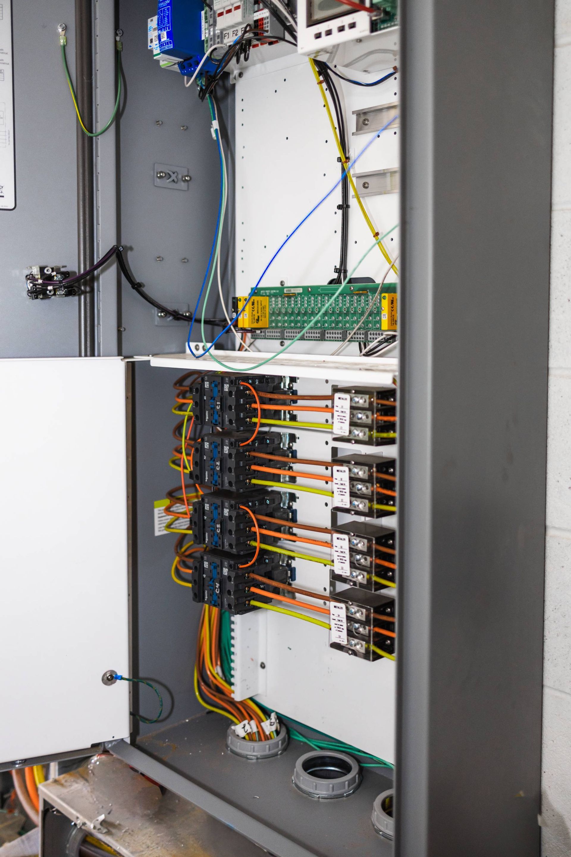 Electrical control panel with wires and circuit breakers; open door reveals interior.