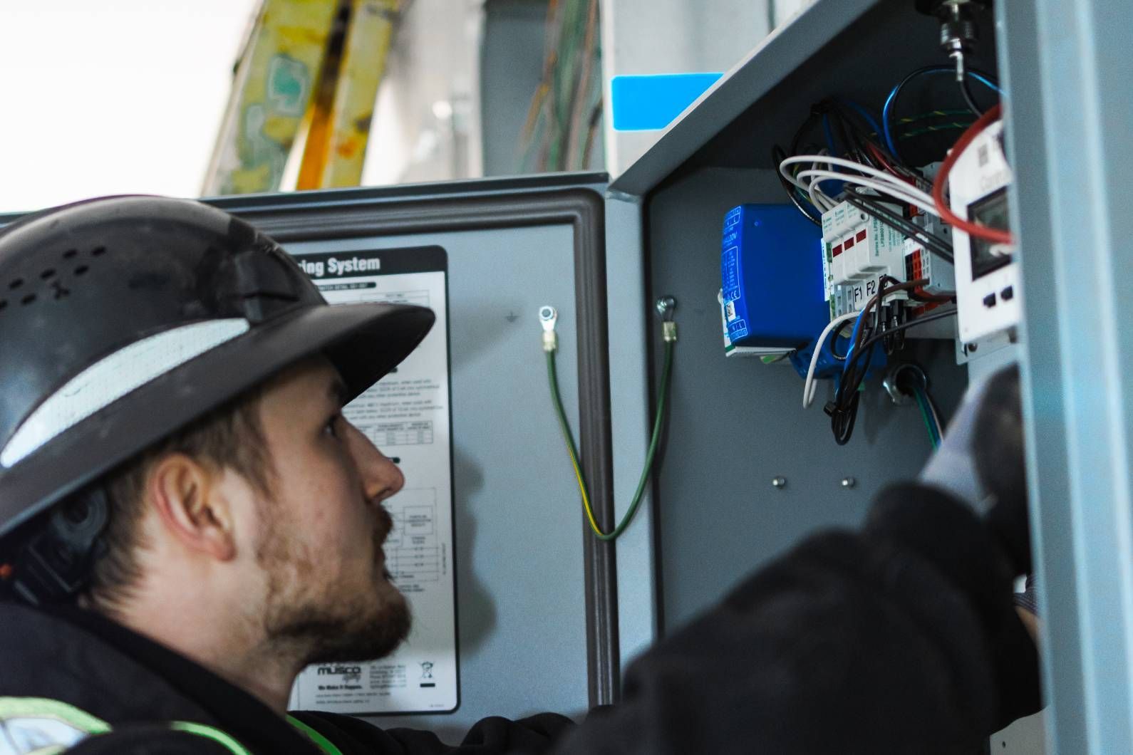 Electrician in hard hat working on electrical panel.