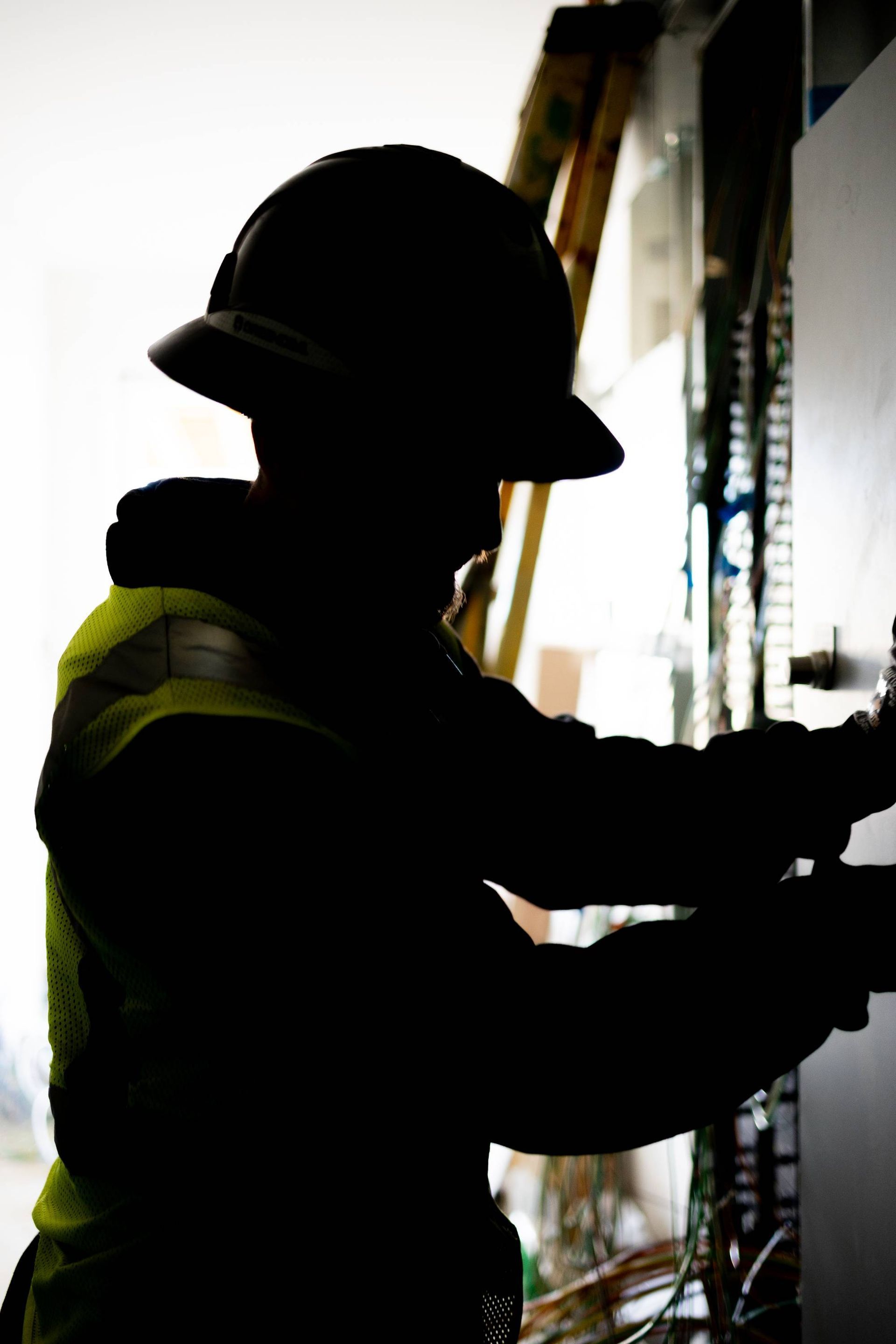 Silhouette of worker in hard hat and safety vest, working with machinery.