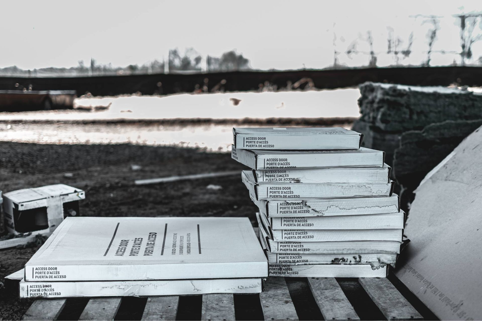 Stack of white boxes with text on a wooden pallet outdoors, near water.
