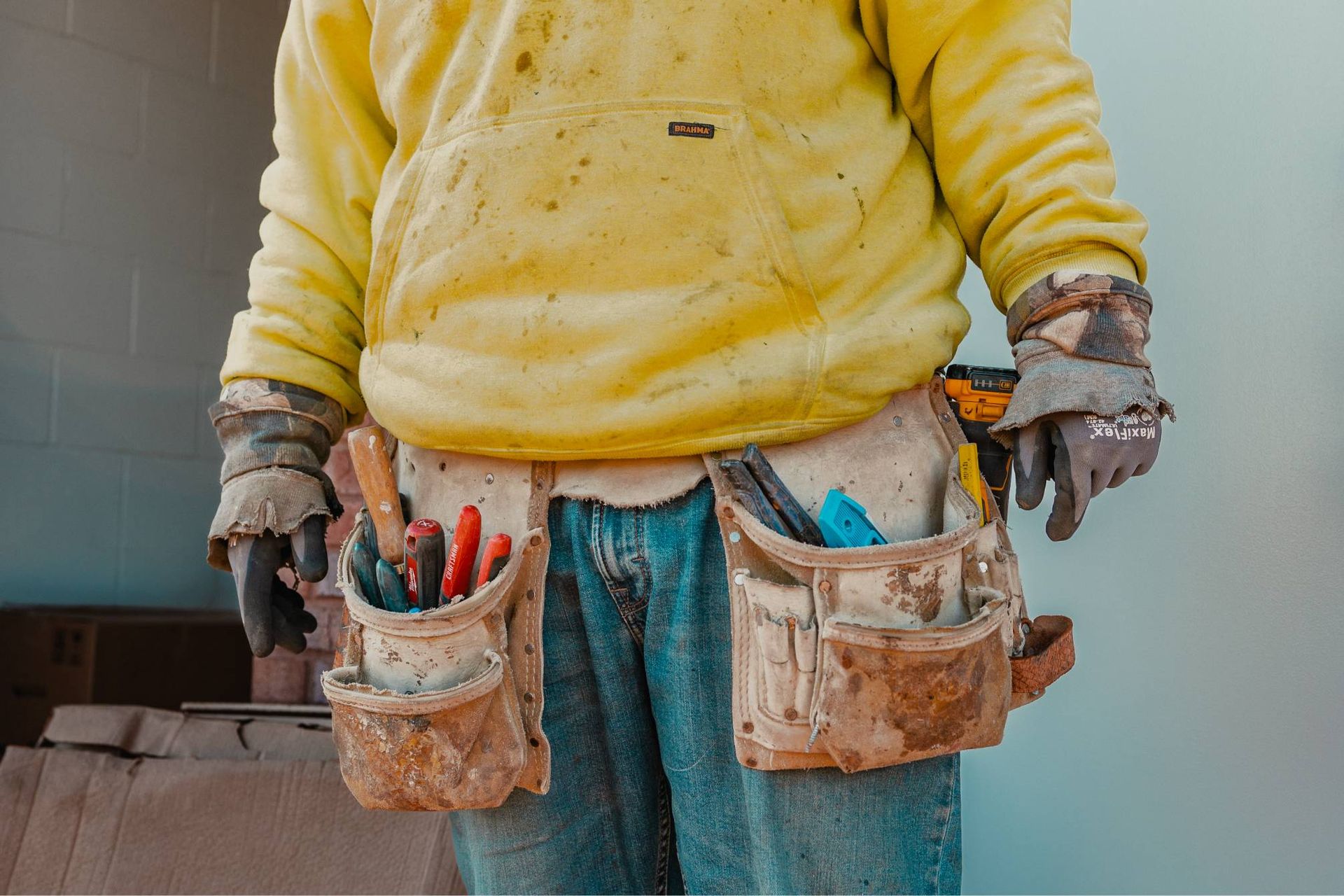 Worker in yellow hoodie and tool belt, holding tools.