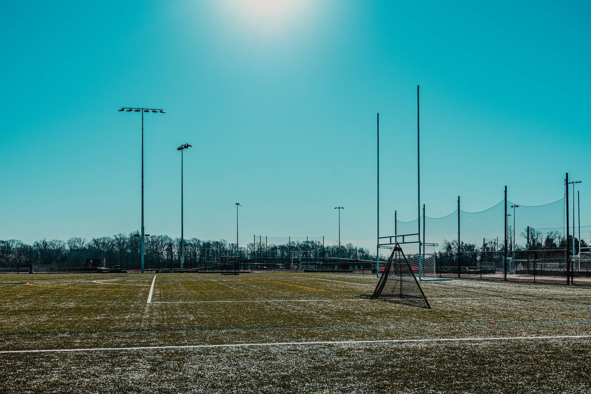 Soccer field with goalposts and floodlights against a bright blue sky.