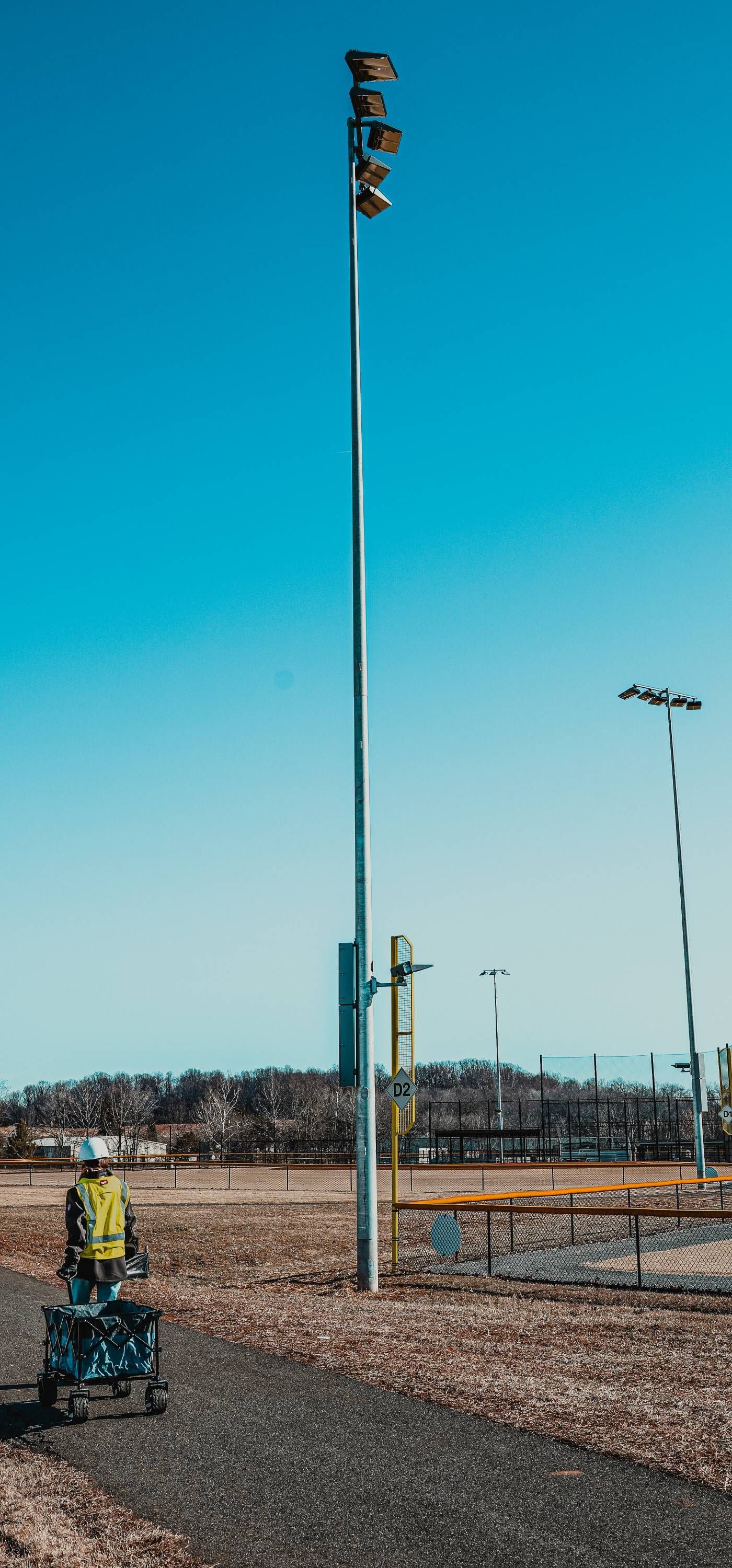 Person using a walker on a pathway near a light pole under a clear, blue sky.