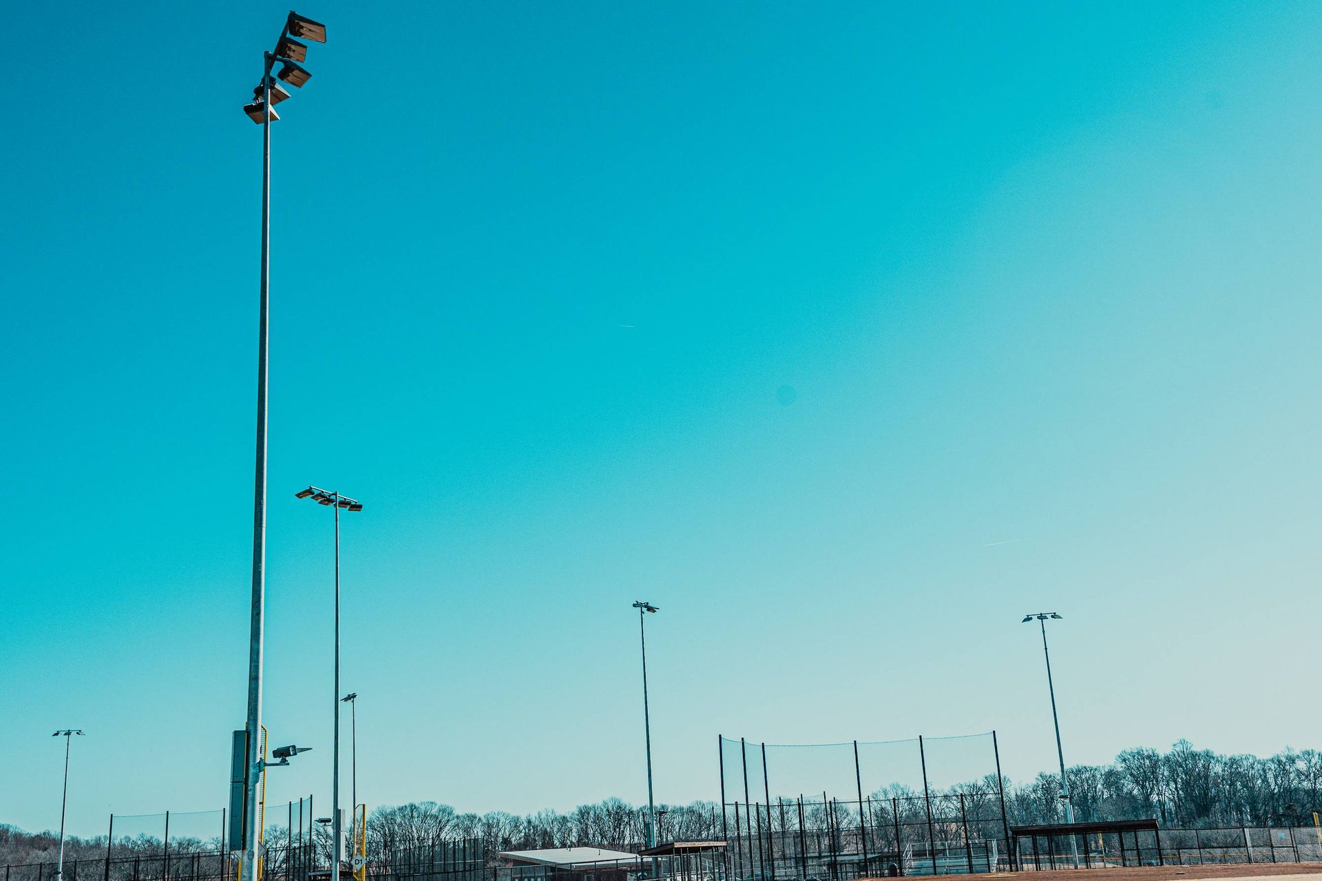 Bright blue sky over a sports field with tall light poles and netting.