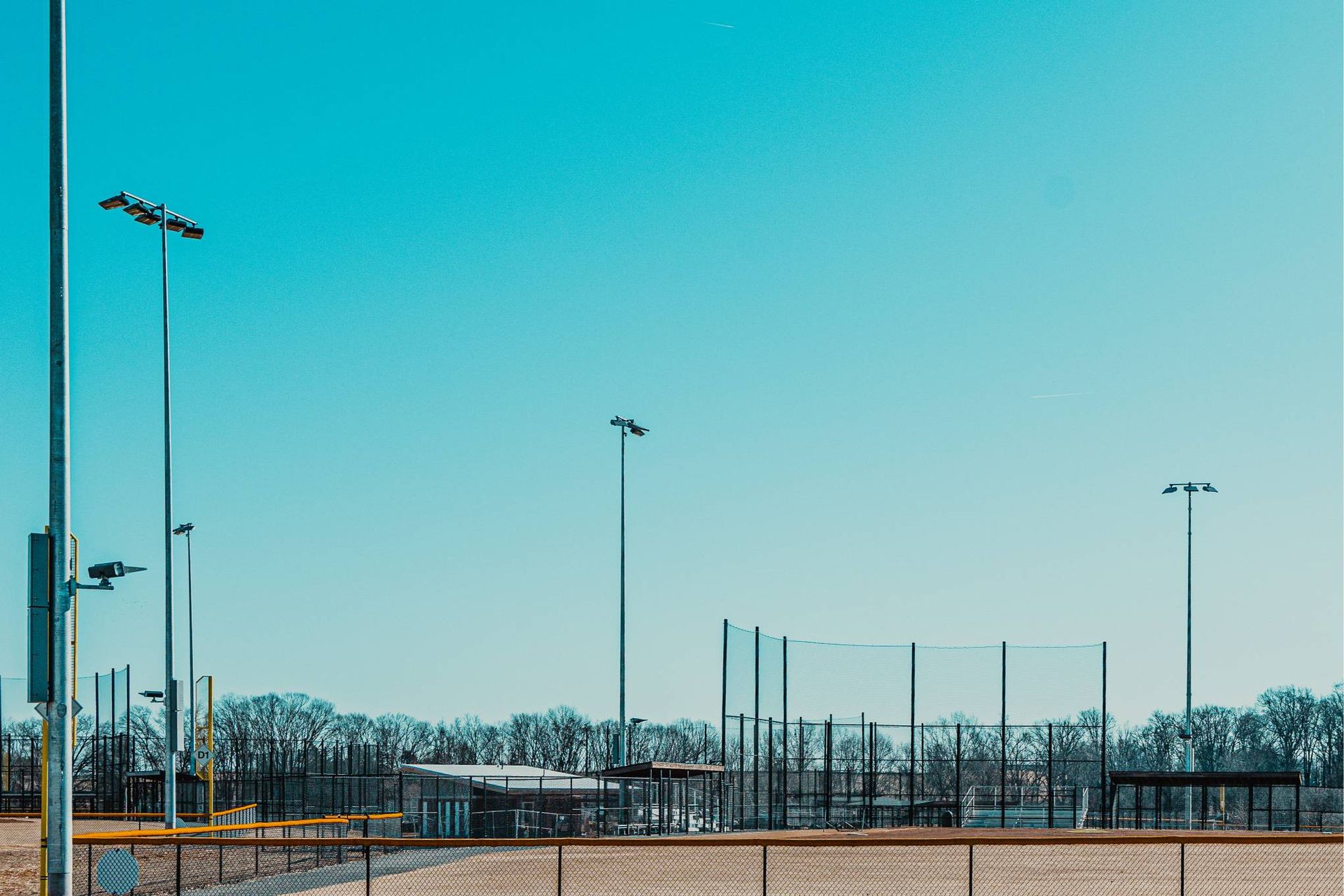 Empty baseball field on a sunny day with tall light poles and a clear blue sky.