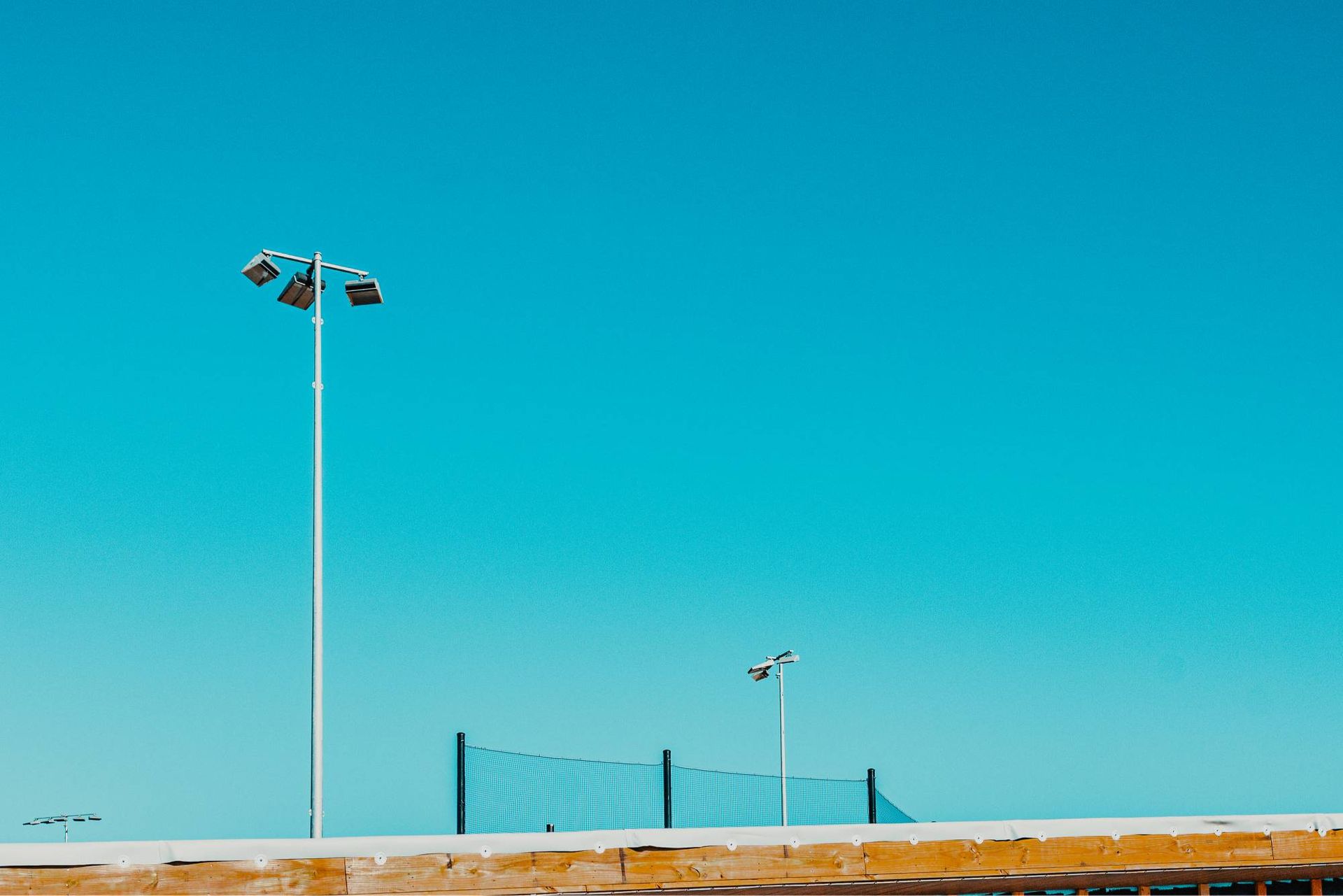 Blue sky over a tennis net, two light poles, and a yellow wall.