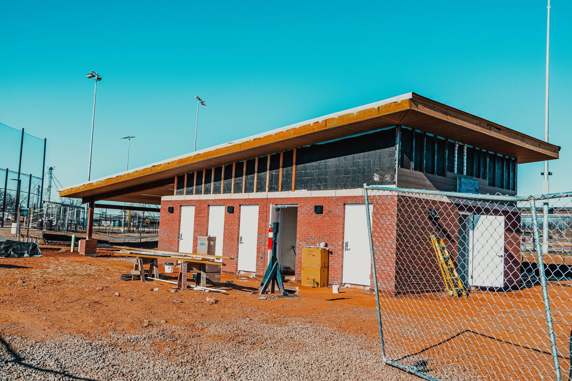 Baseball field building under construction with red brick exterior, white doors, and a long wooden roof.