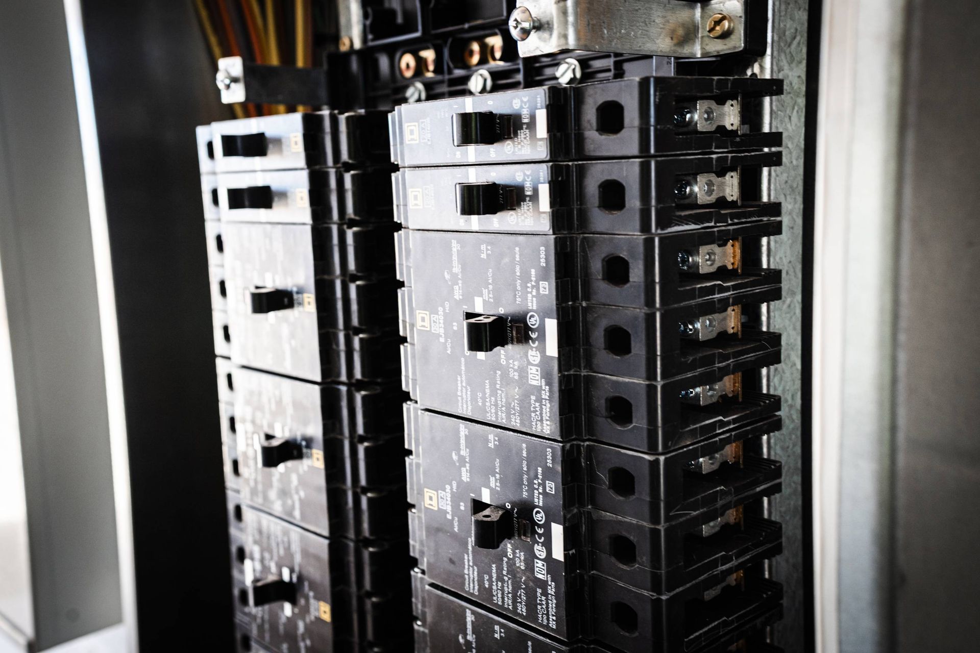 Black electrical circuit breakers stacked inside a metal panel.