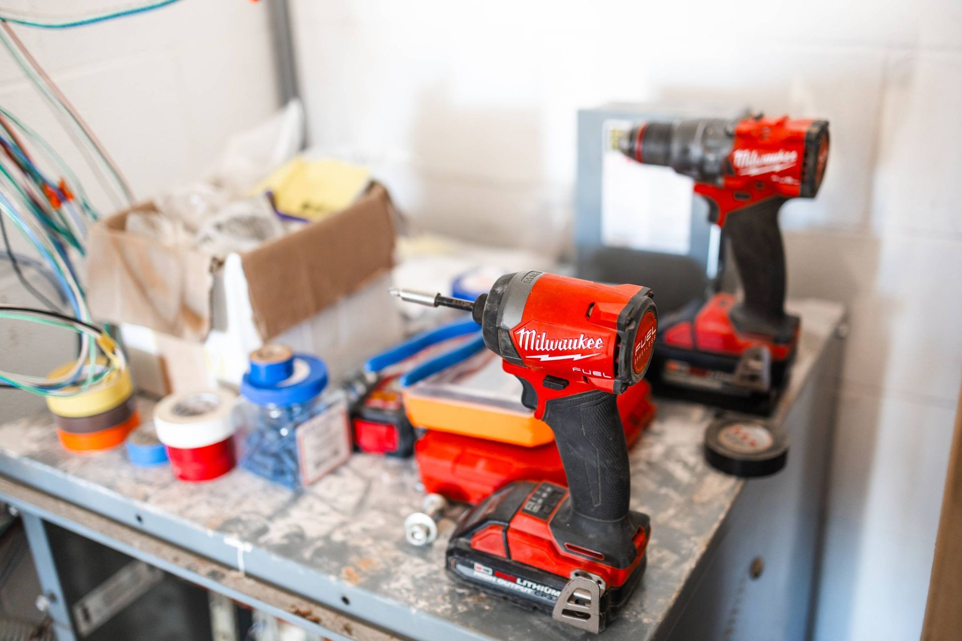 Two red power drills, a box of supplies, and tools on a metal workbench.