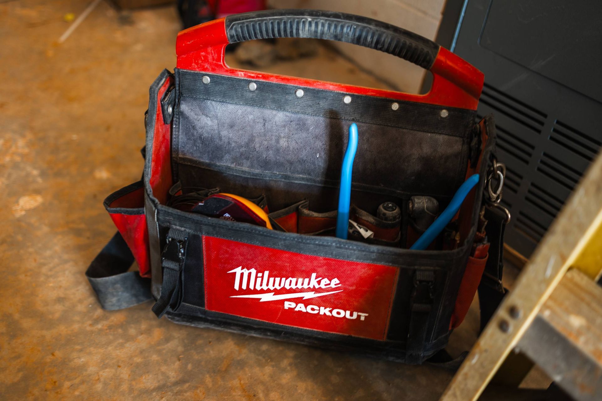 Red and black Milwaukee Packout tool bag with tools inside, sitting on the floor.
