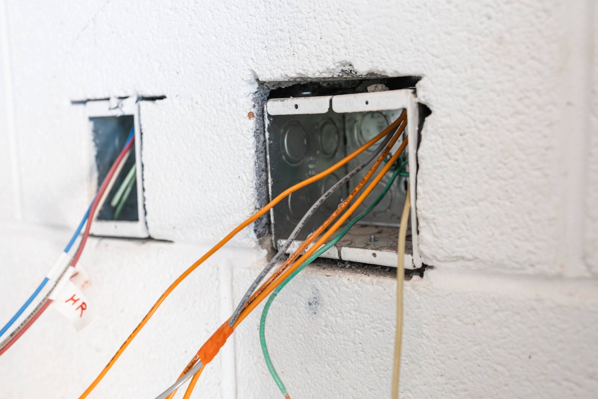 Electrical boxes with exposed wires in a white wall during construction.