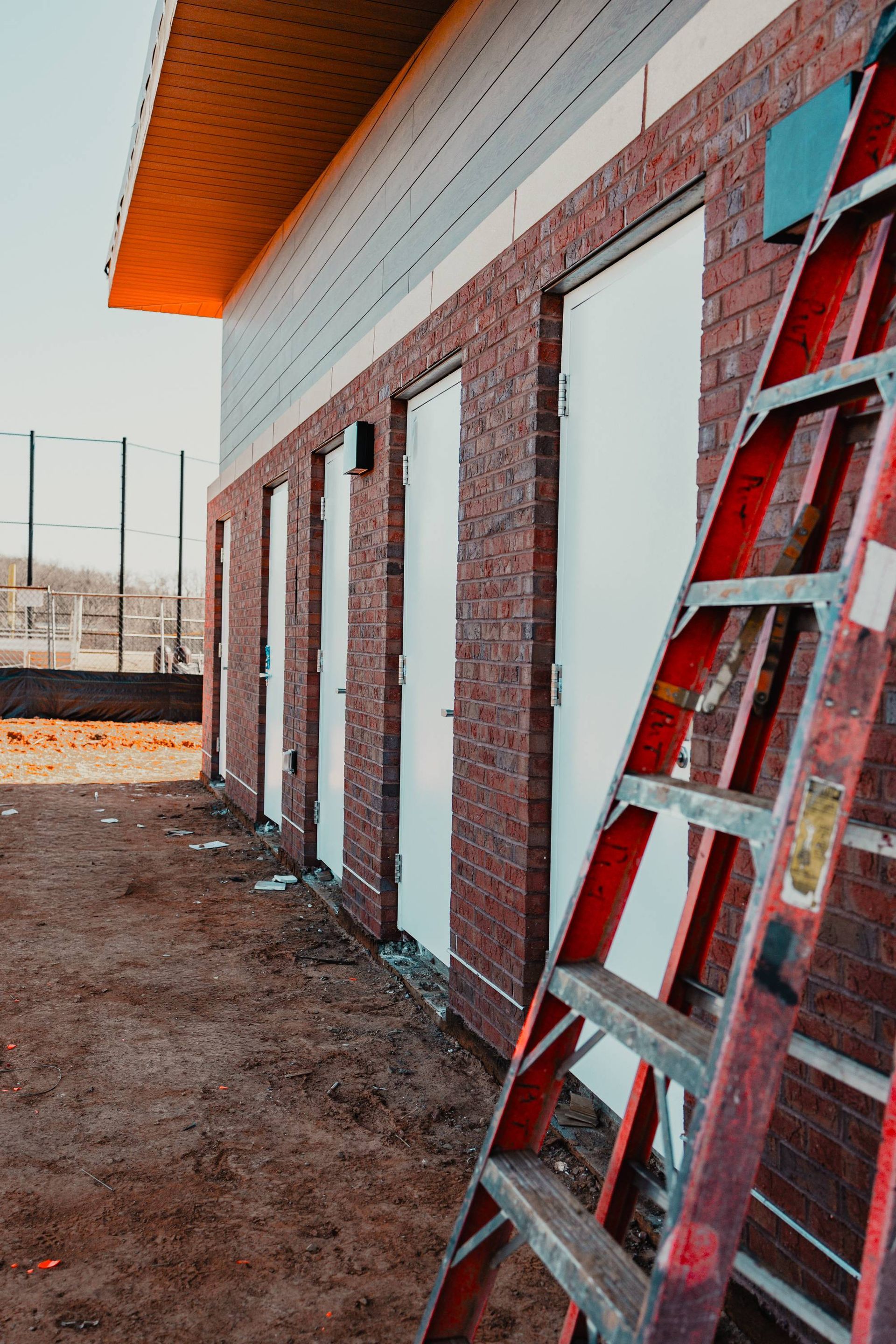 Red brick building with white doors and a red ladder leaning against it.