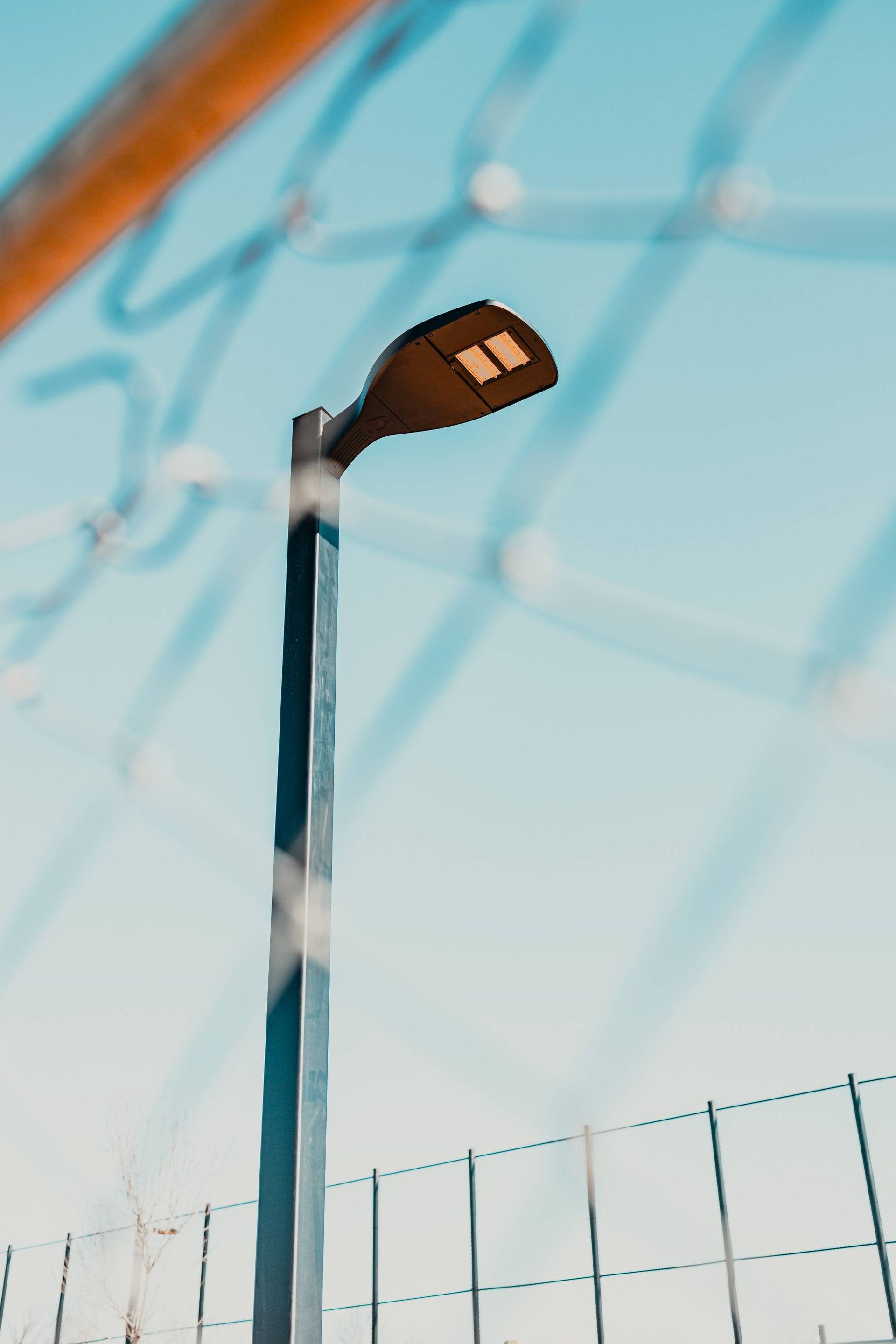 Street lamp behind chain link fence against a blue sky.