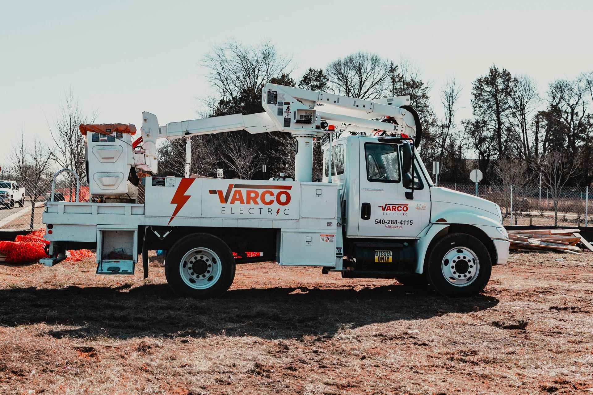 White Varco utility truck with a boom lift in a field on a sunny day.