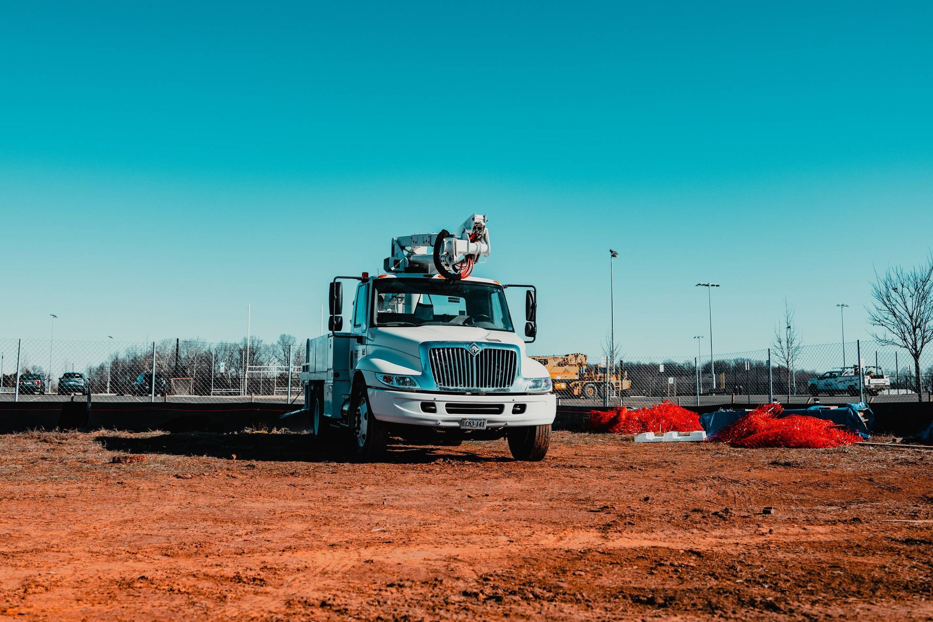 White truck with a crane parked on dirt field; blue sky in the background.