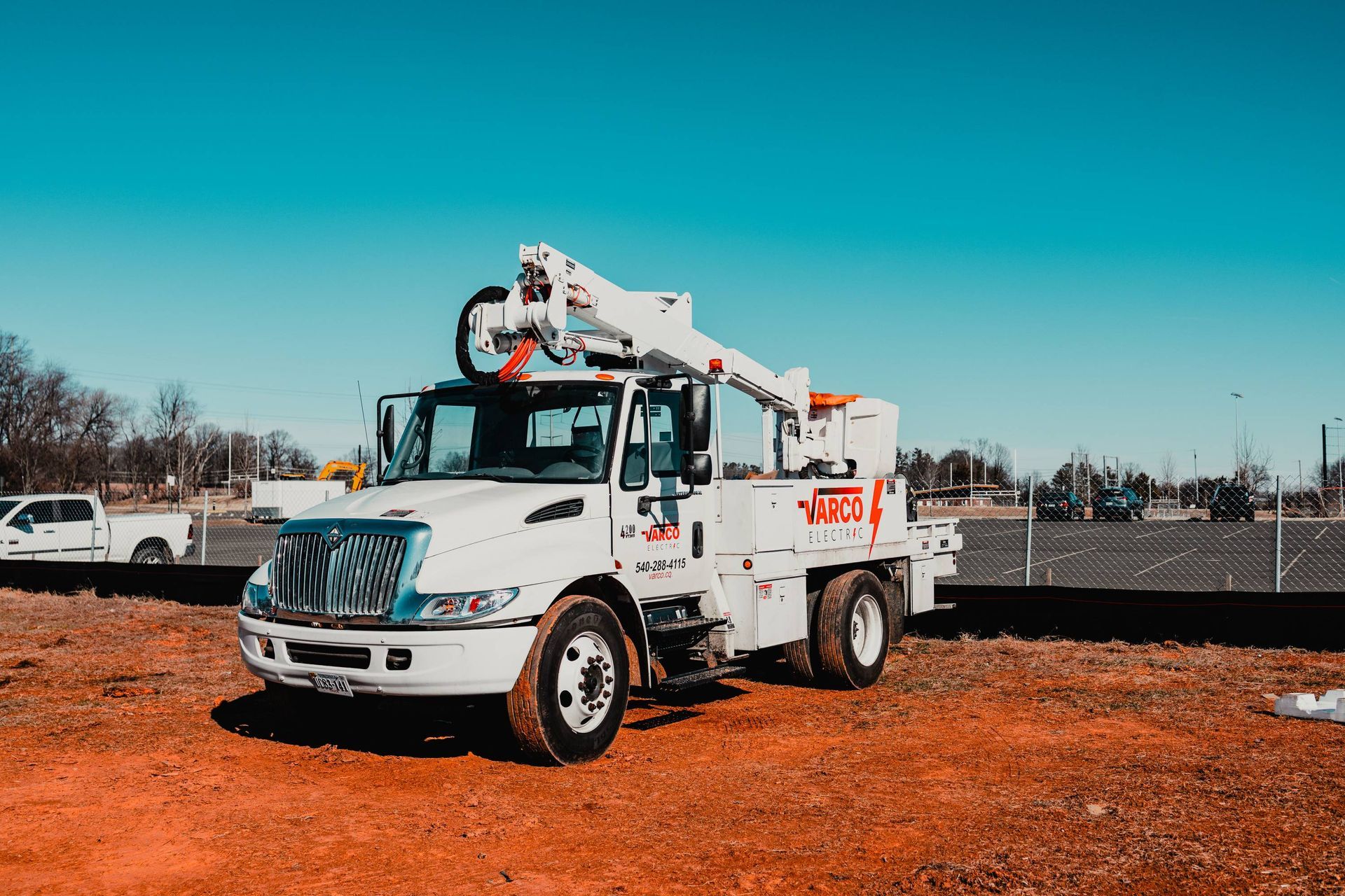 White utility truck with an extended boom on red dirt under a blue sky.