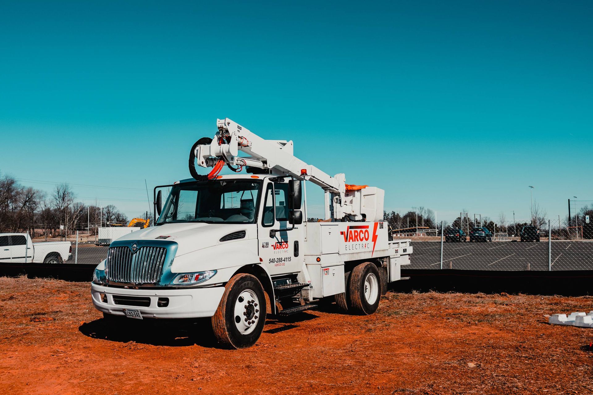 White utility truck with an extended boom, parked on red dirt under a blue sky.