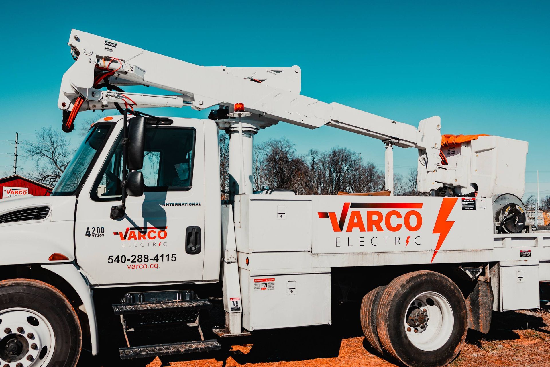 White Varco Electric truck with elevated crane arm. Red lightning bolt logo on the side.