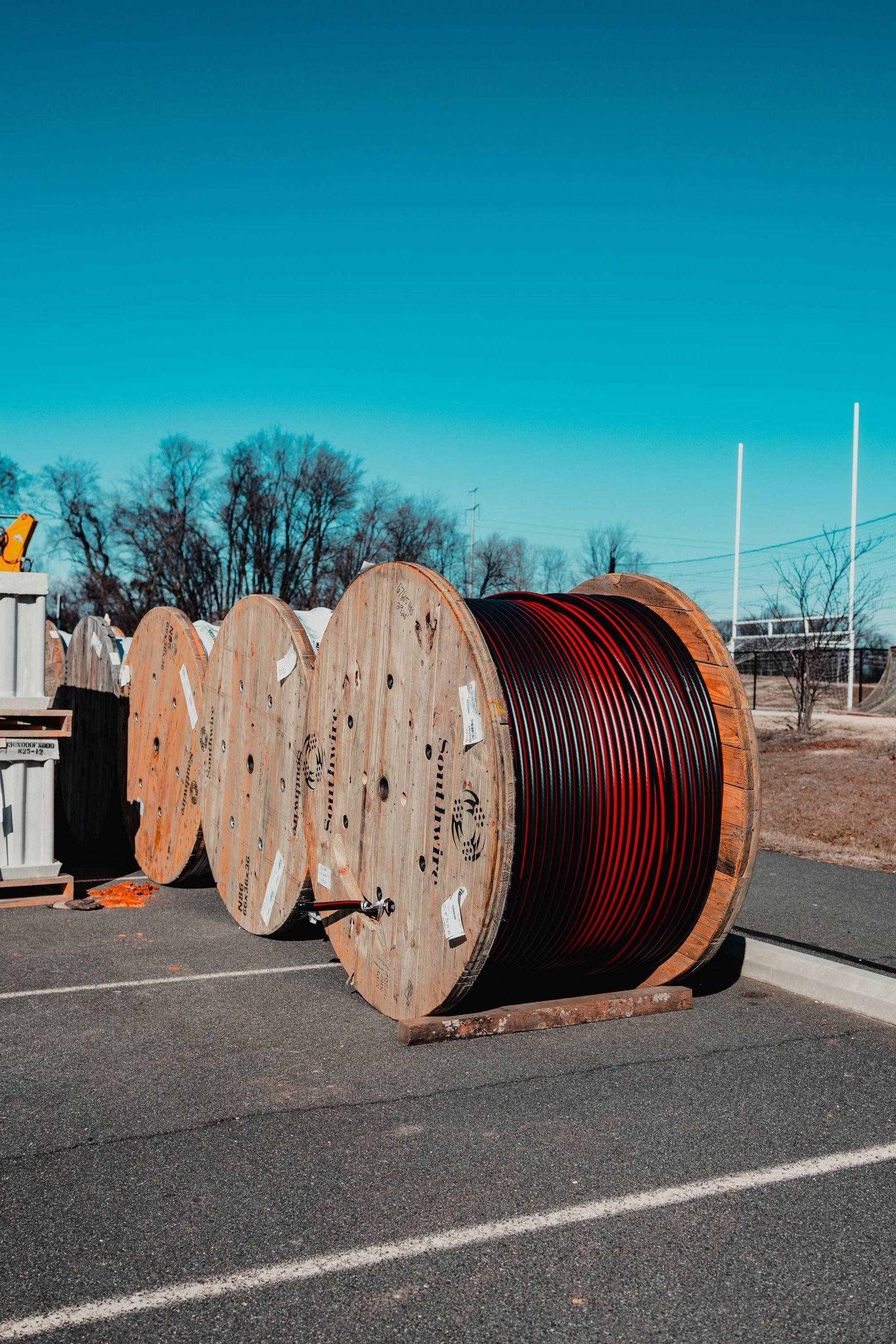 Wooden spools of wire on asphalt, with a blue sky background.