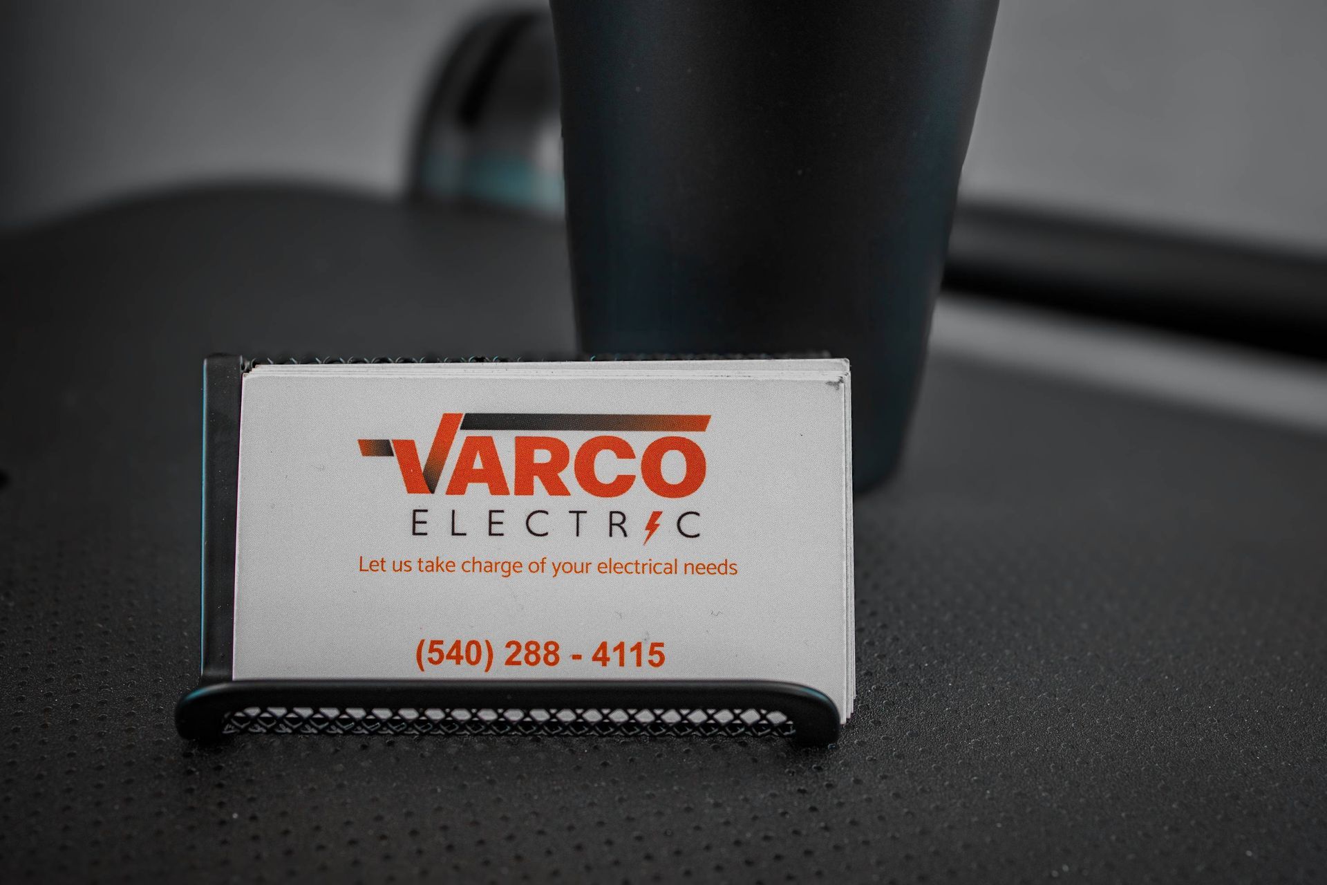 Business card for Varco Electric in a holder, phone number visible, next to a black mug.