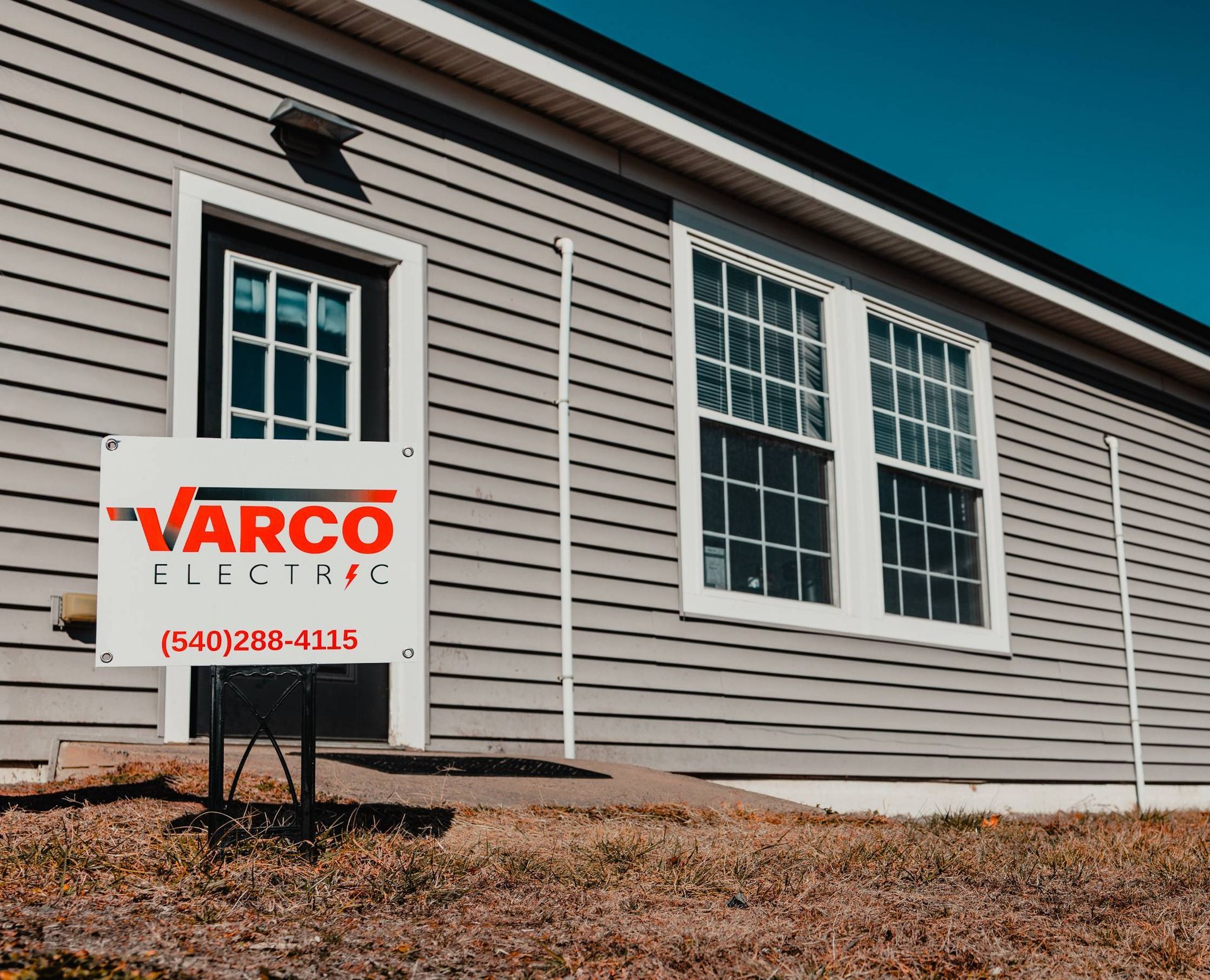 Sign for Varco Electric in front of a gray building with windows and a door.