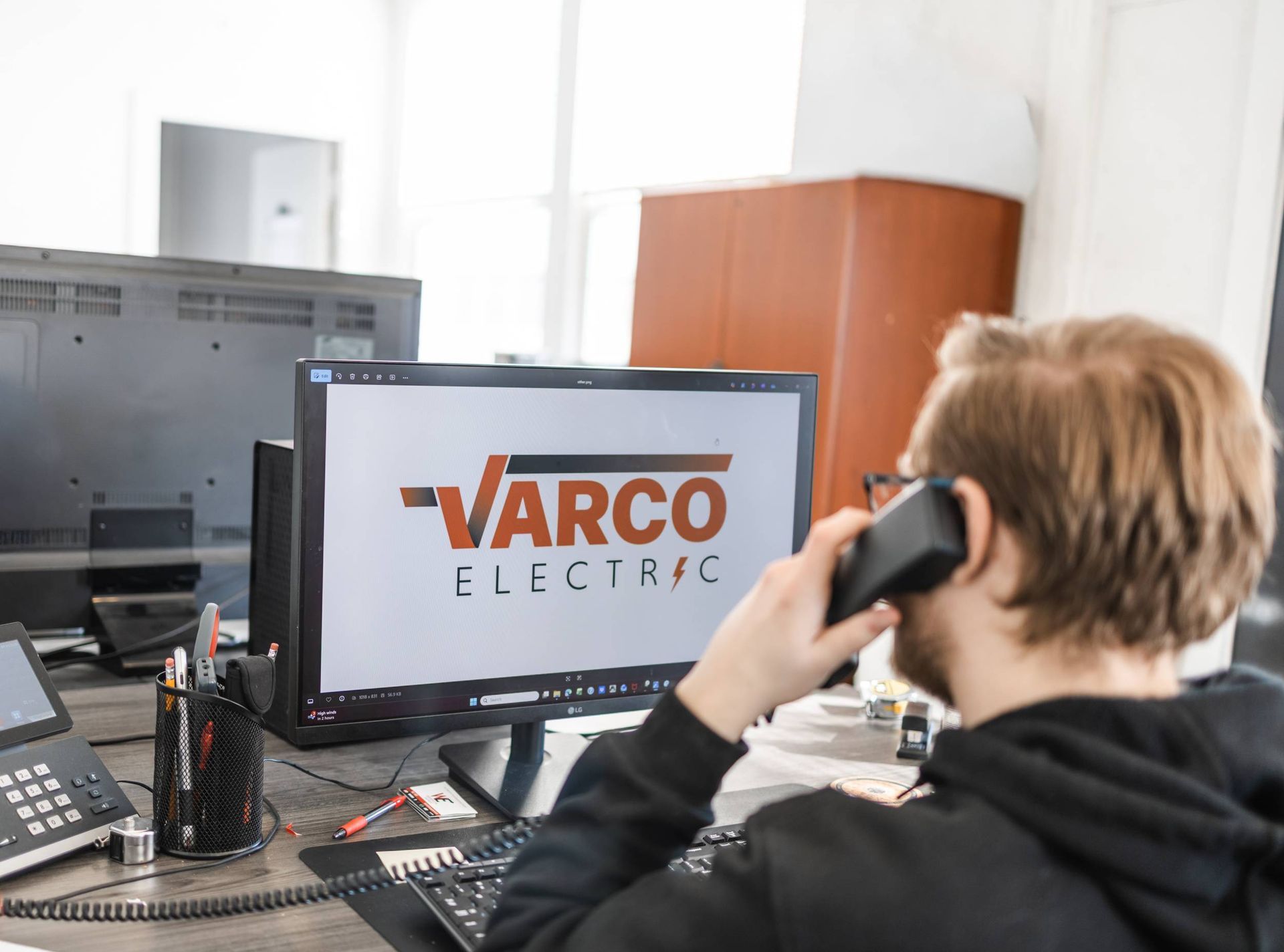 Man on phone in office; computer screen shows VARCO ELECTRIC logo.