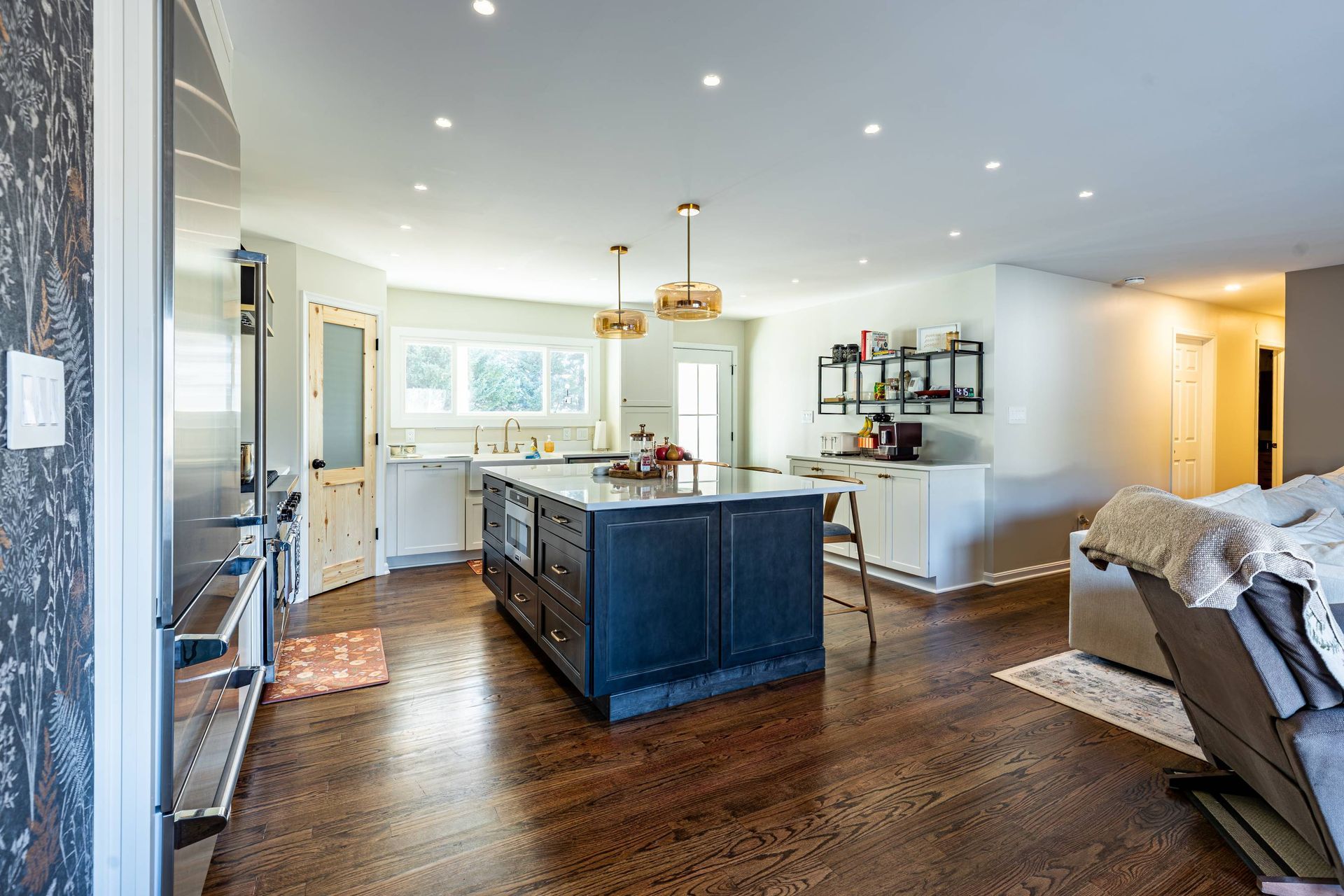 Spacious kitchen with dark blue island, white cabinets, hardwood floors, and overhead lighting.