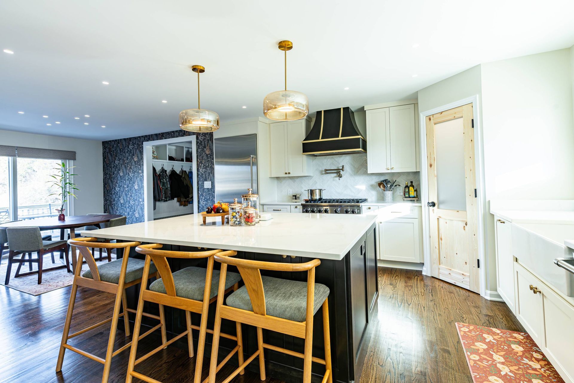 Modern kitchen with island, seating, and gold pendant lights. Dark cabinets, white counters, and wood floors.