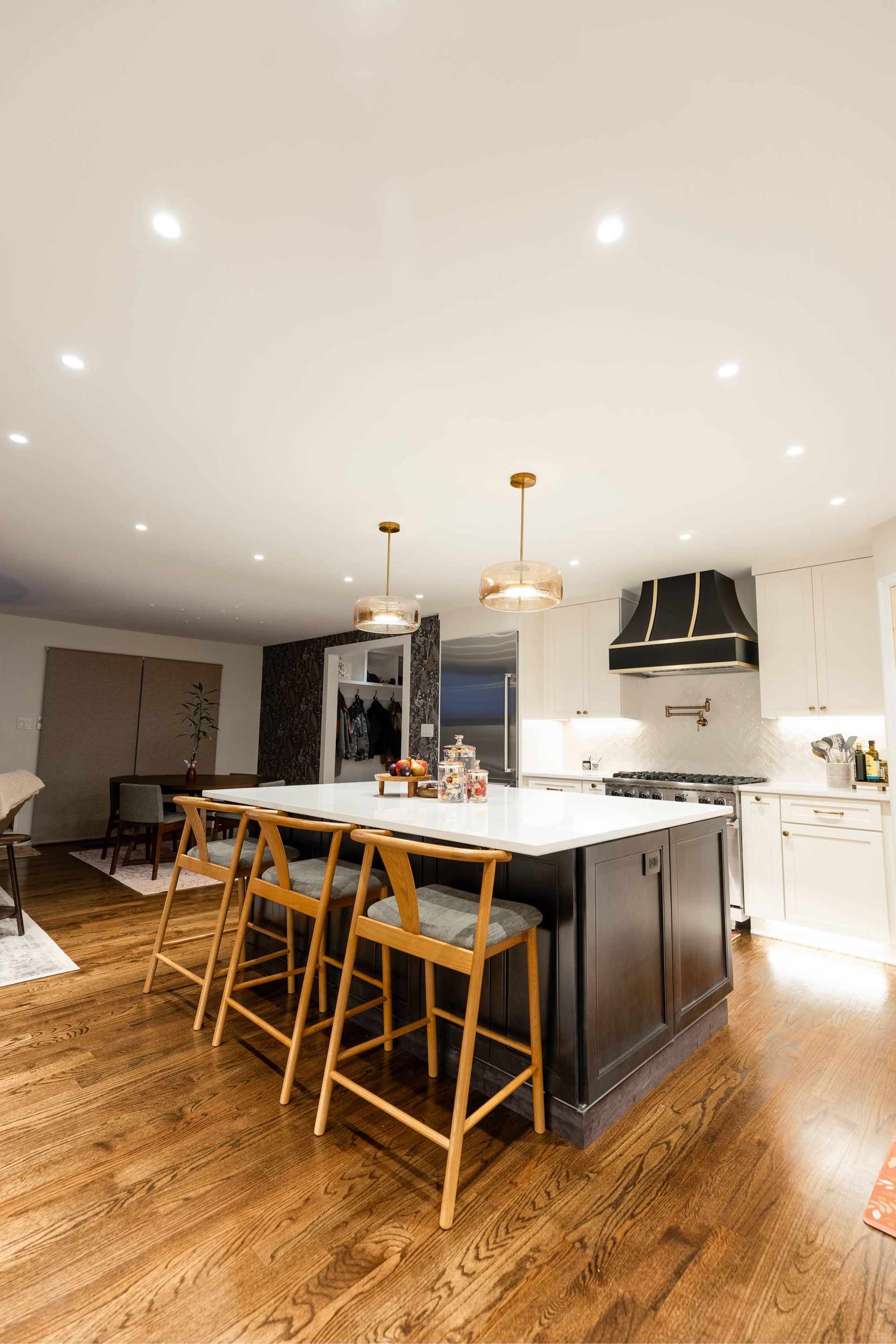 Kitchen with island seating, dark cabinets, white countertops, and hardwood floors.
