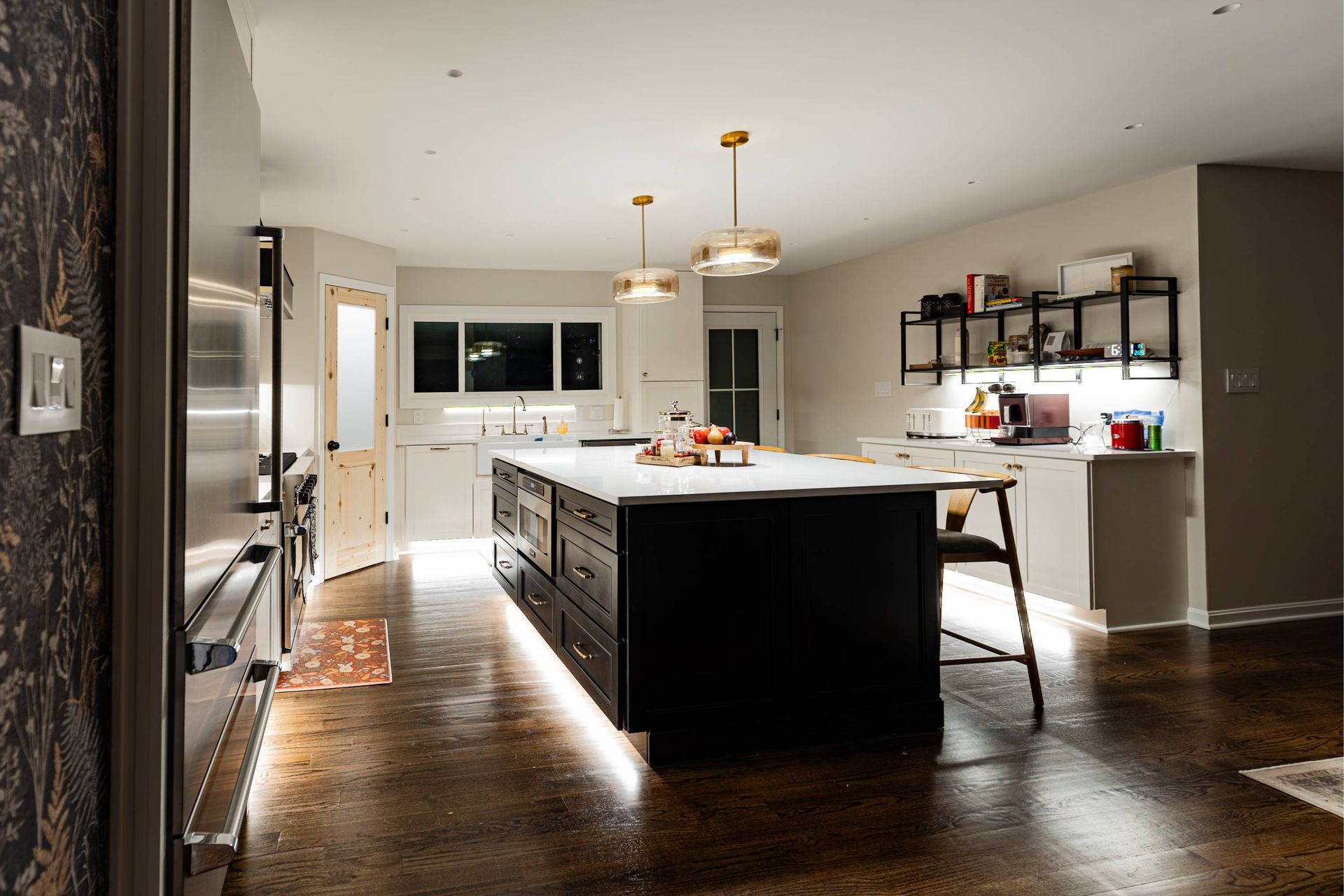 Modern kitchen with black island, white countertop, and under-cabinet lighting.