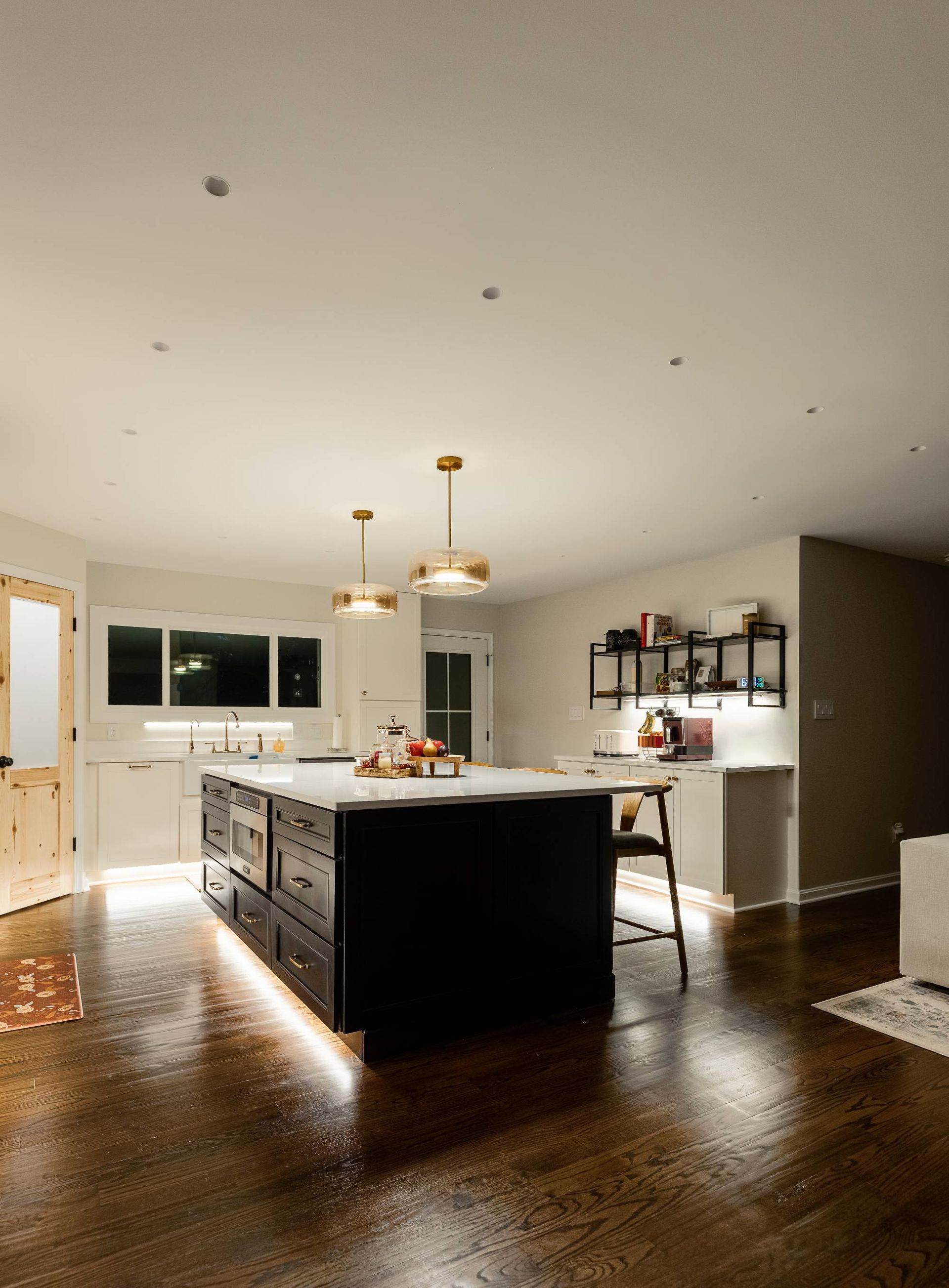 Modern kitchen with dark island, white cabinets, and wood floors.