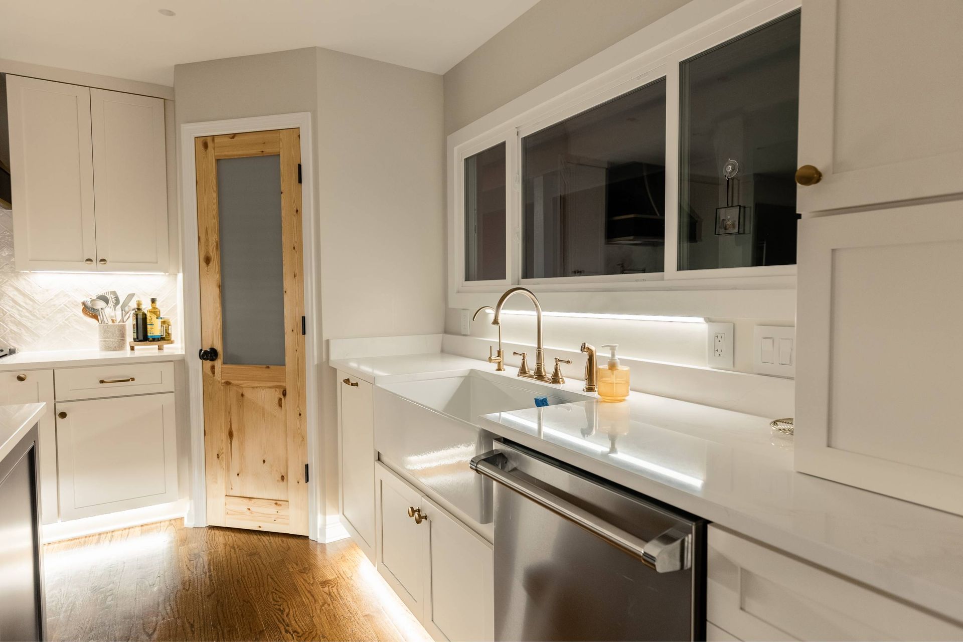 Bright kitchen with white cabinets, stainless steel dishwasher, and a wood-paneled door.