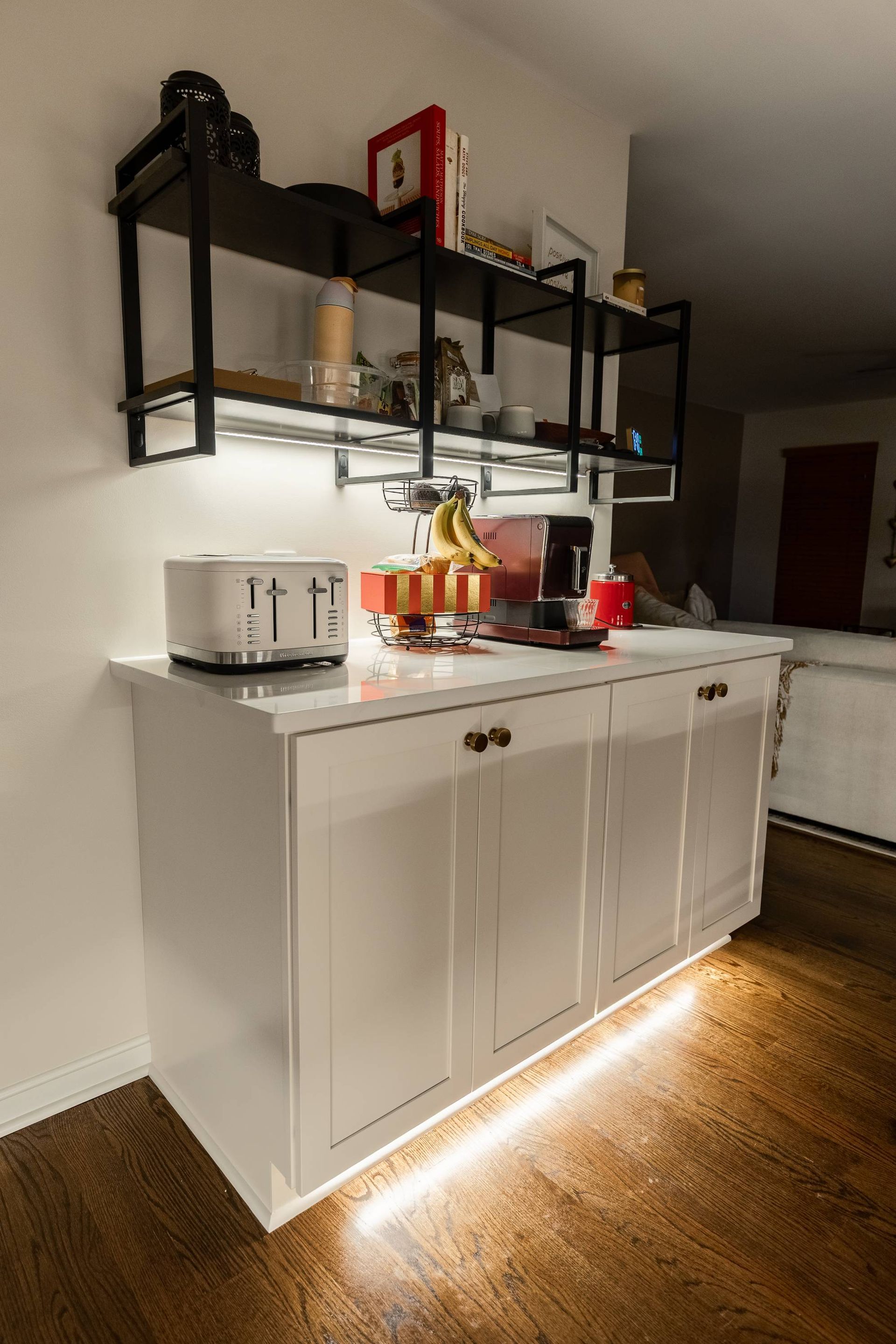 White cabinet with open shelves above; countertop with appliances and food. Illuminated with lights.