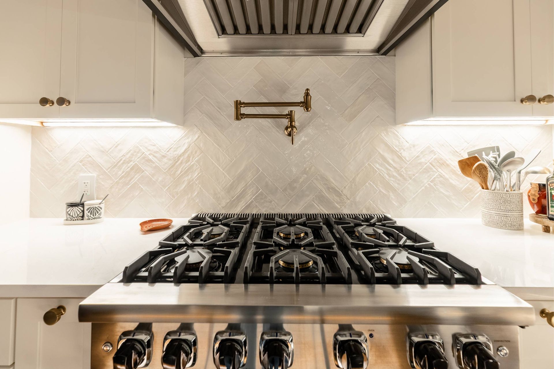 Stainless steel stove and white cabinets in a bright kitchen with herringbone tile backsplash and gold hardware.
