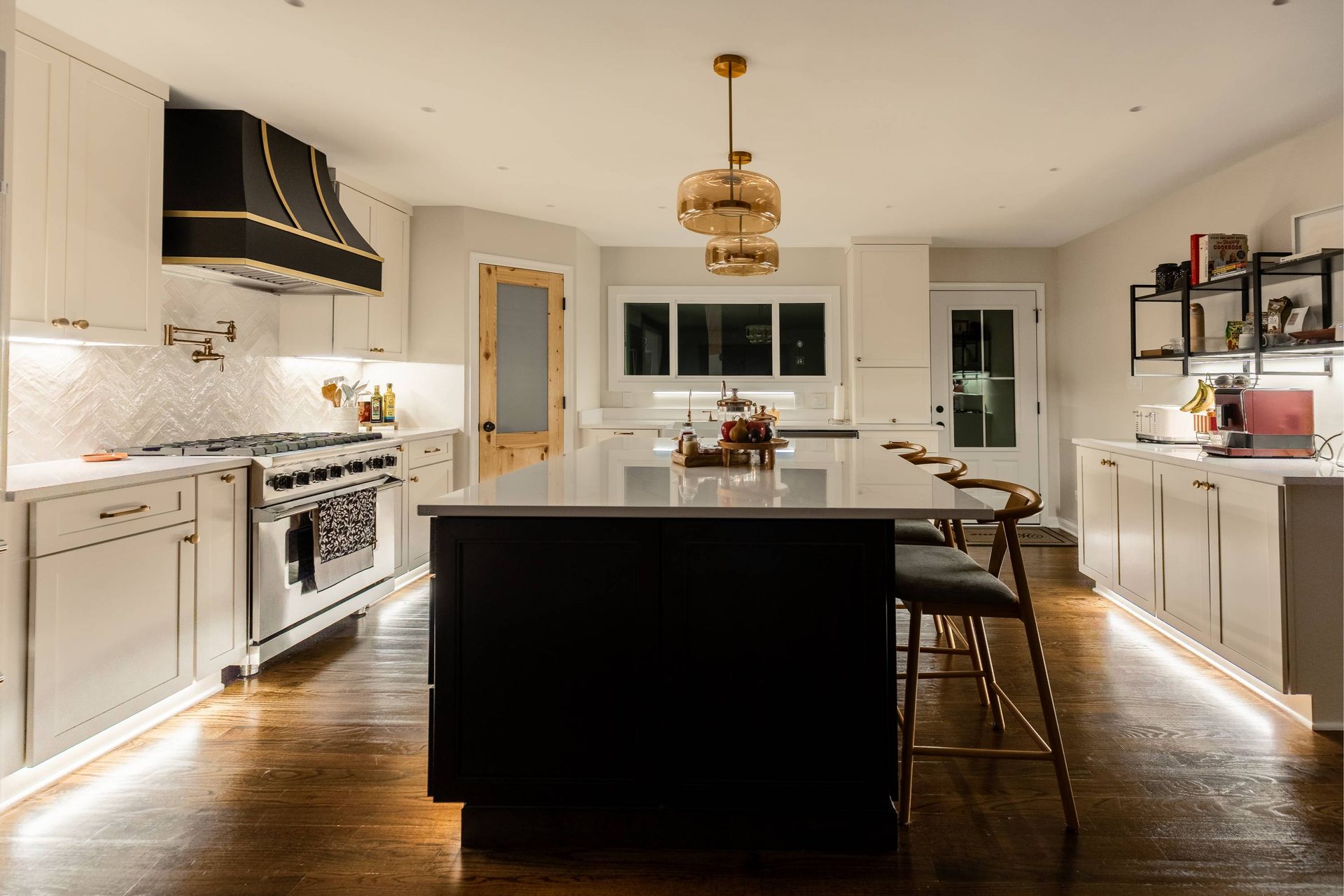 Modern kitchen with black island, white cabinets, and dark wood floor; pendant lights.
