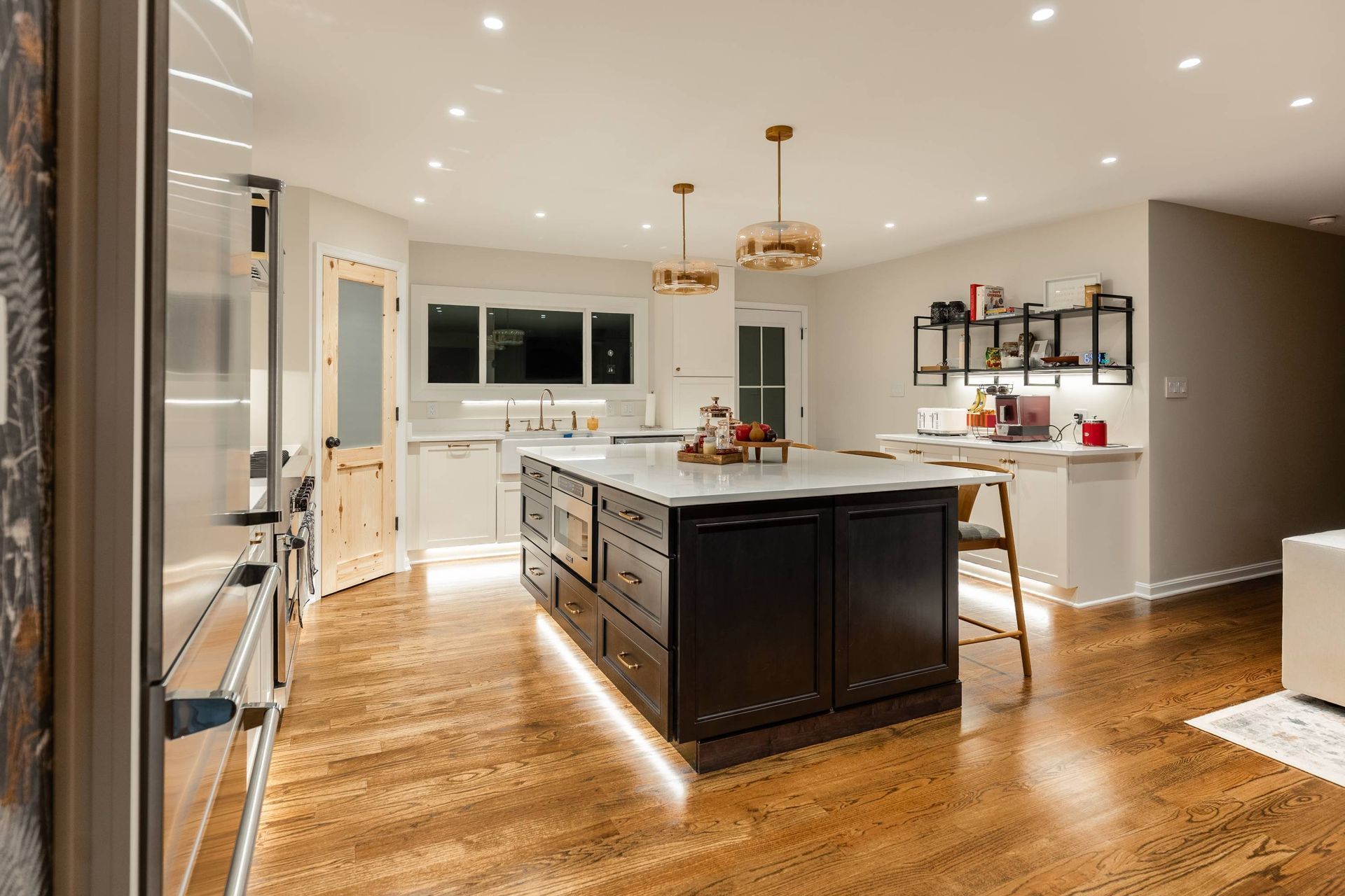 Modern kitchen with dark island, wood floors, and bright lighting.