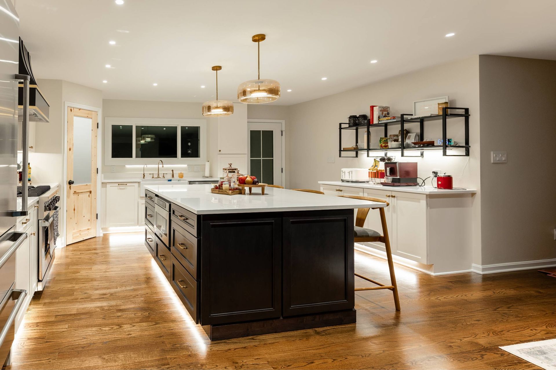 Modern kitchen with a black island, white countertops, and gold pendant lights.