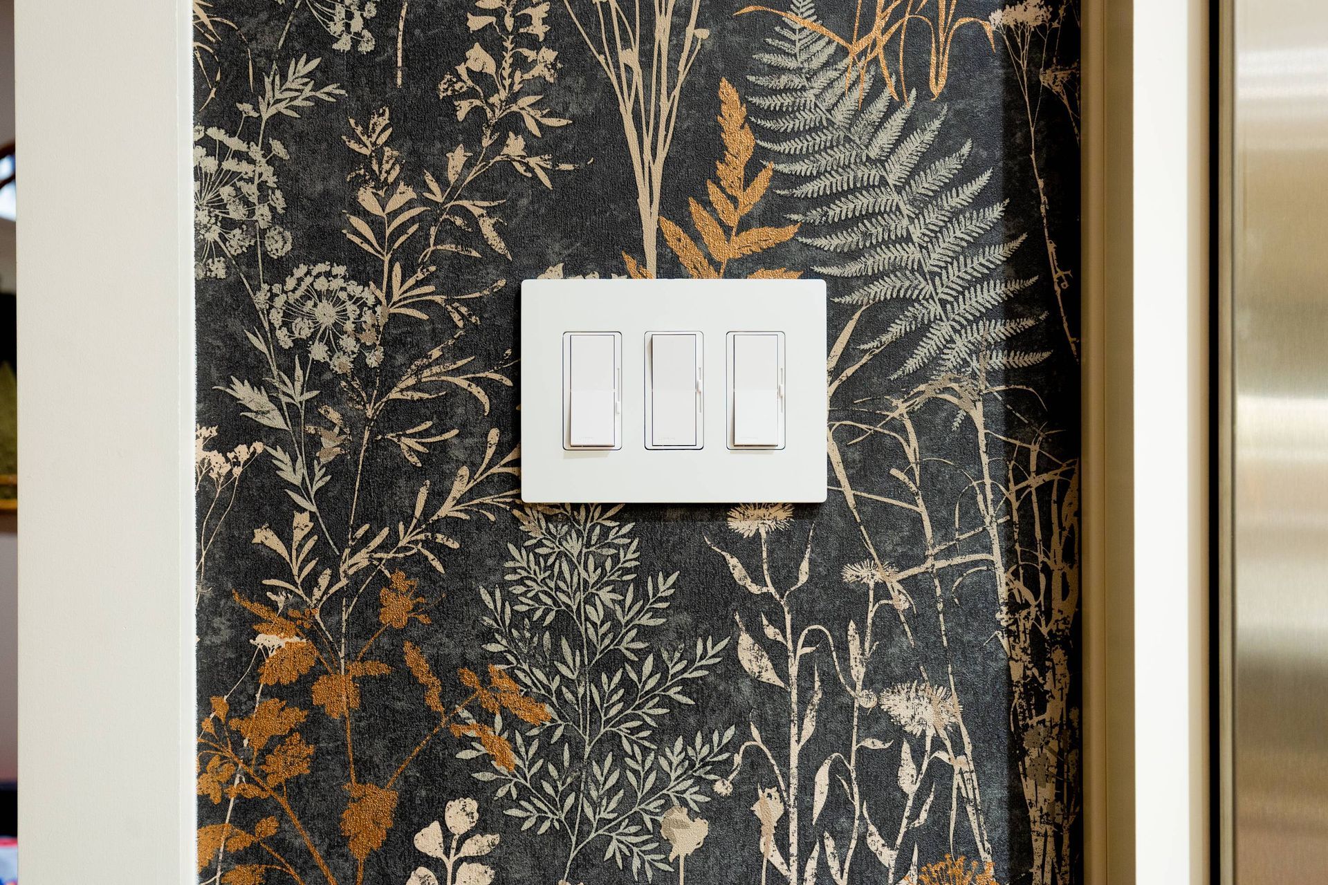 White light switches on patterned botanical wallpaper.