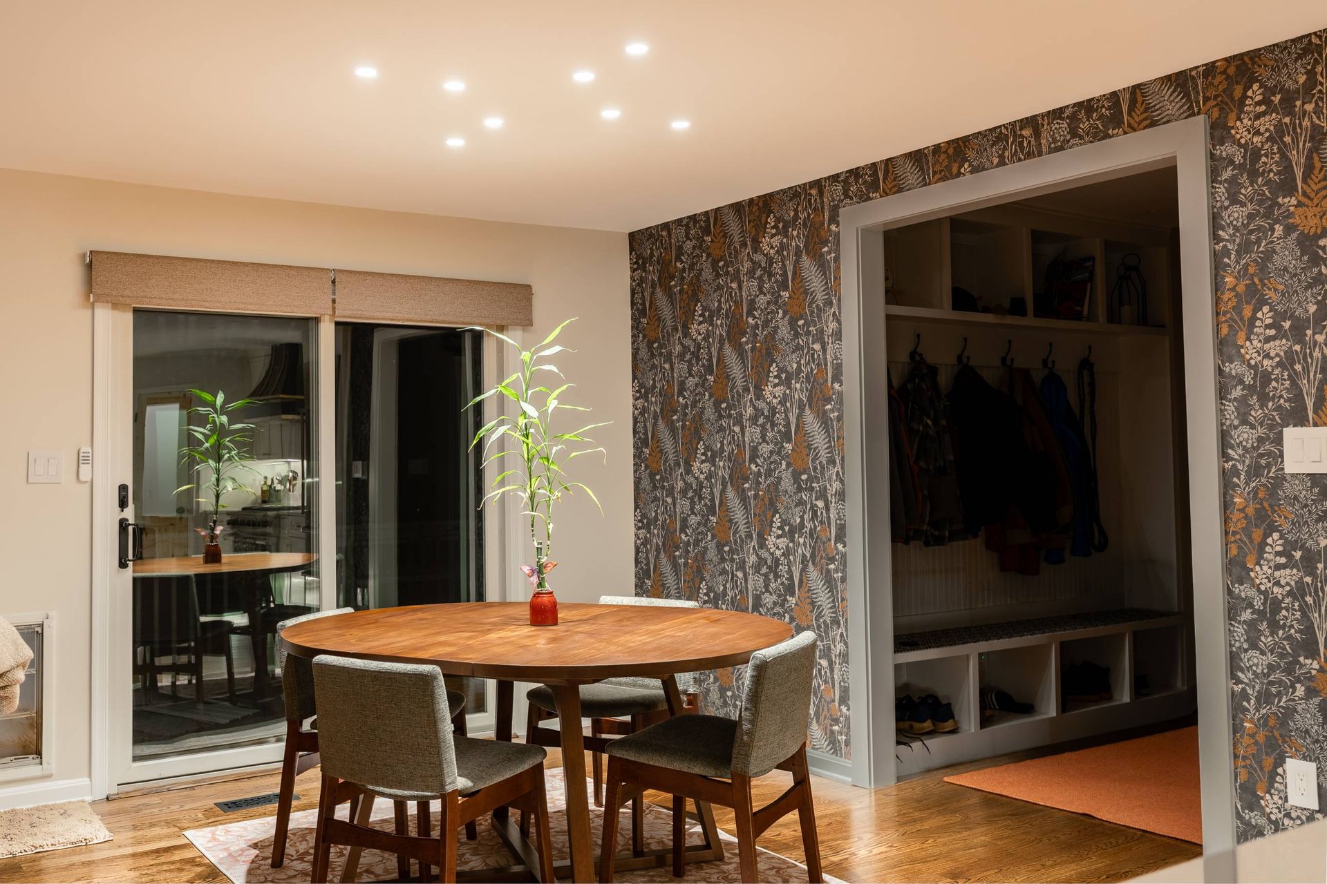 Dining room with wooden table, chairs, and sliding glass door. A patterned accent wall is visible.