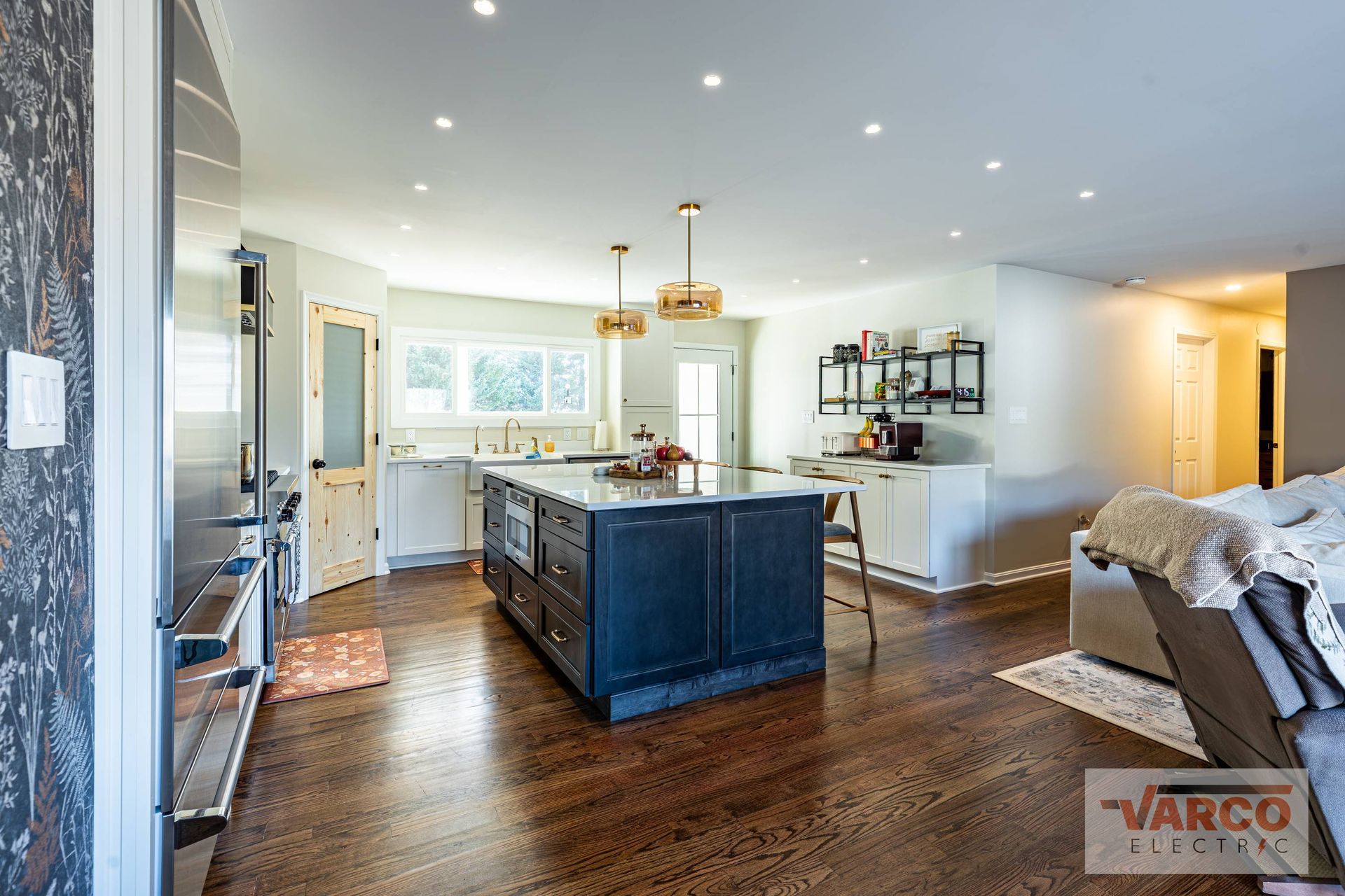 Spacious kitchen with a dark blue island, white cabinets, and wooden floors.