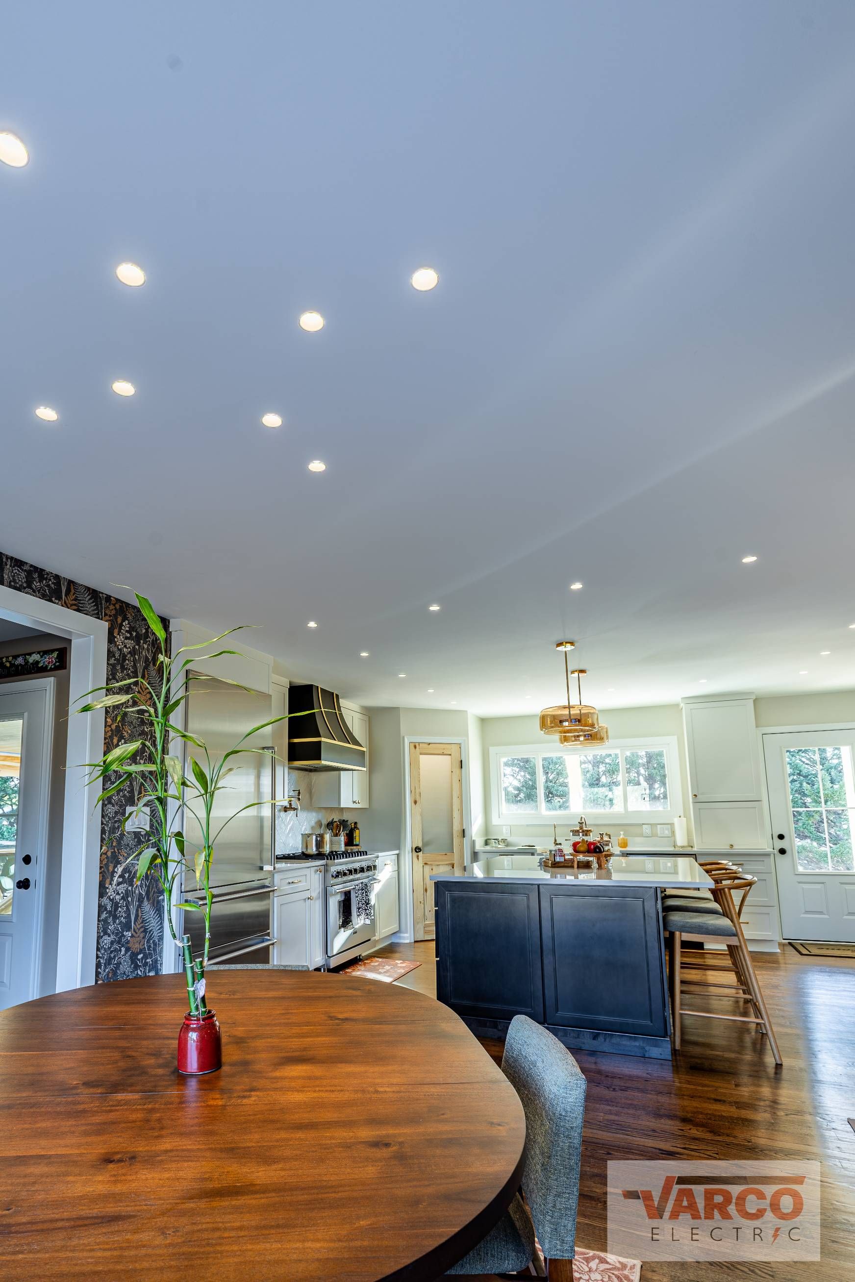 Kitchen interior with island, wood floor, recessed lighting, and a table.
