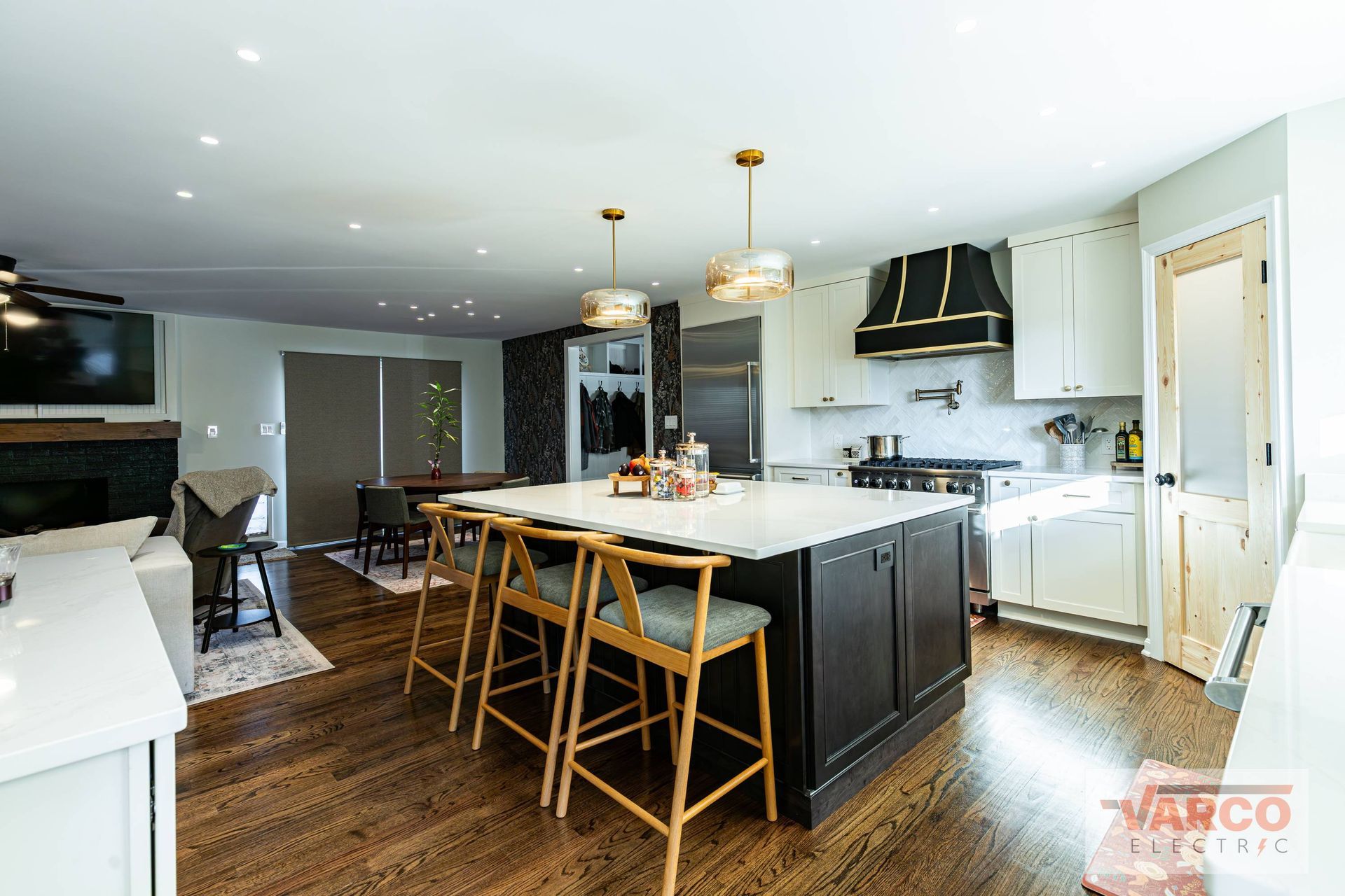 Modern kitchen with dark island, white counters, wood floors, and gold pendant lights.