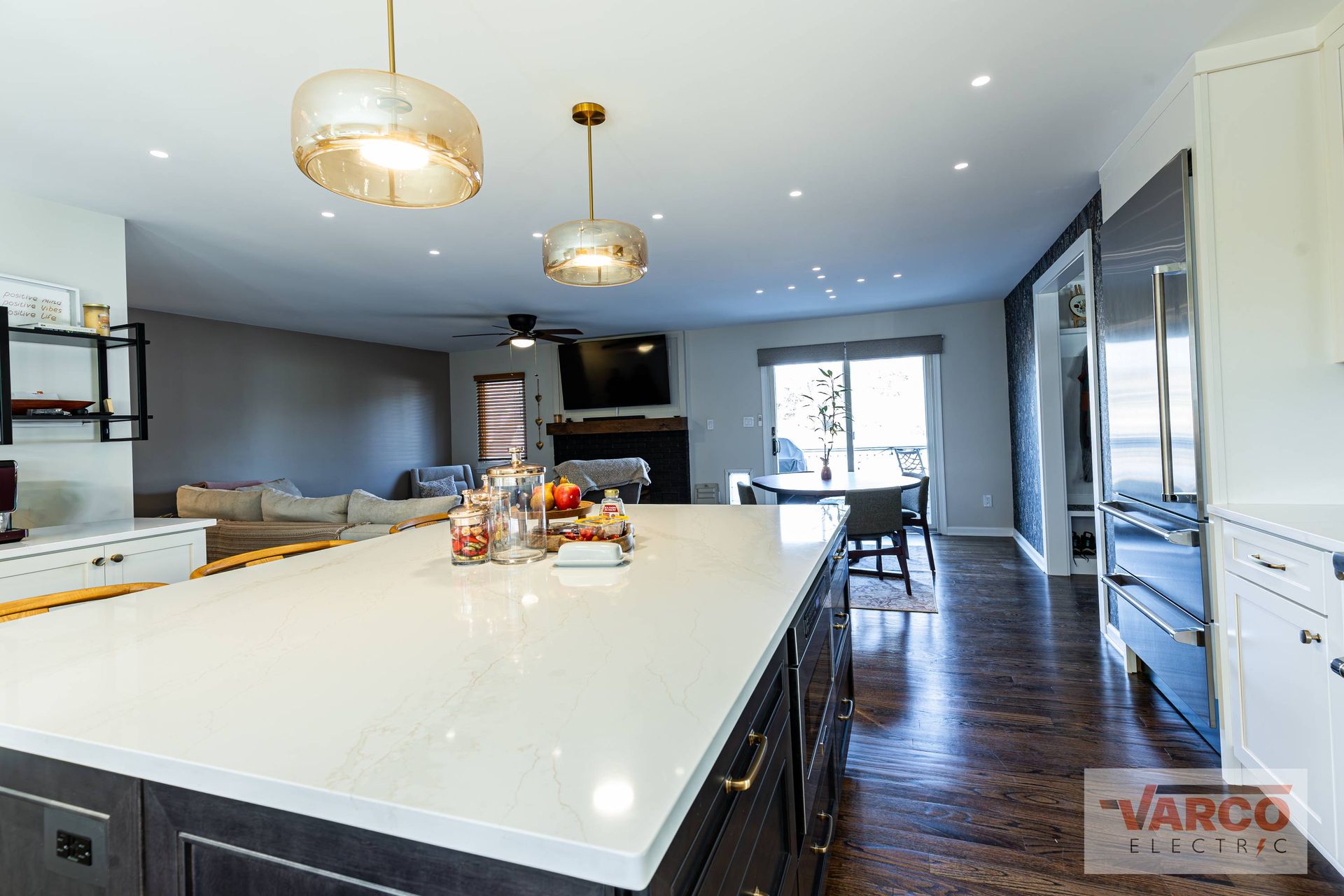 Modern kitchen and living space with island, pendant lights, and dark wood floors.