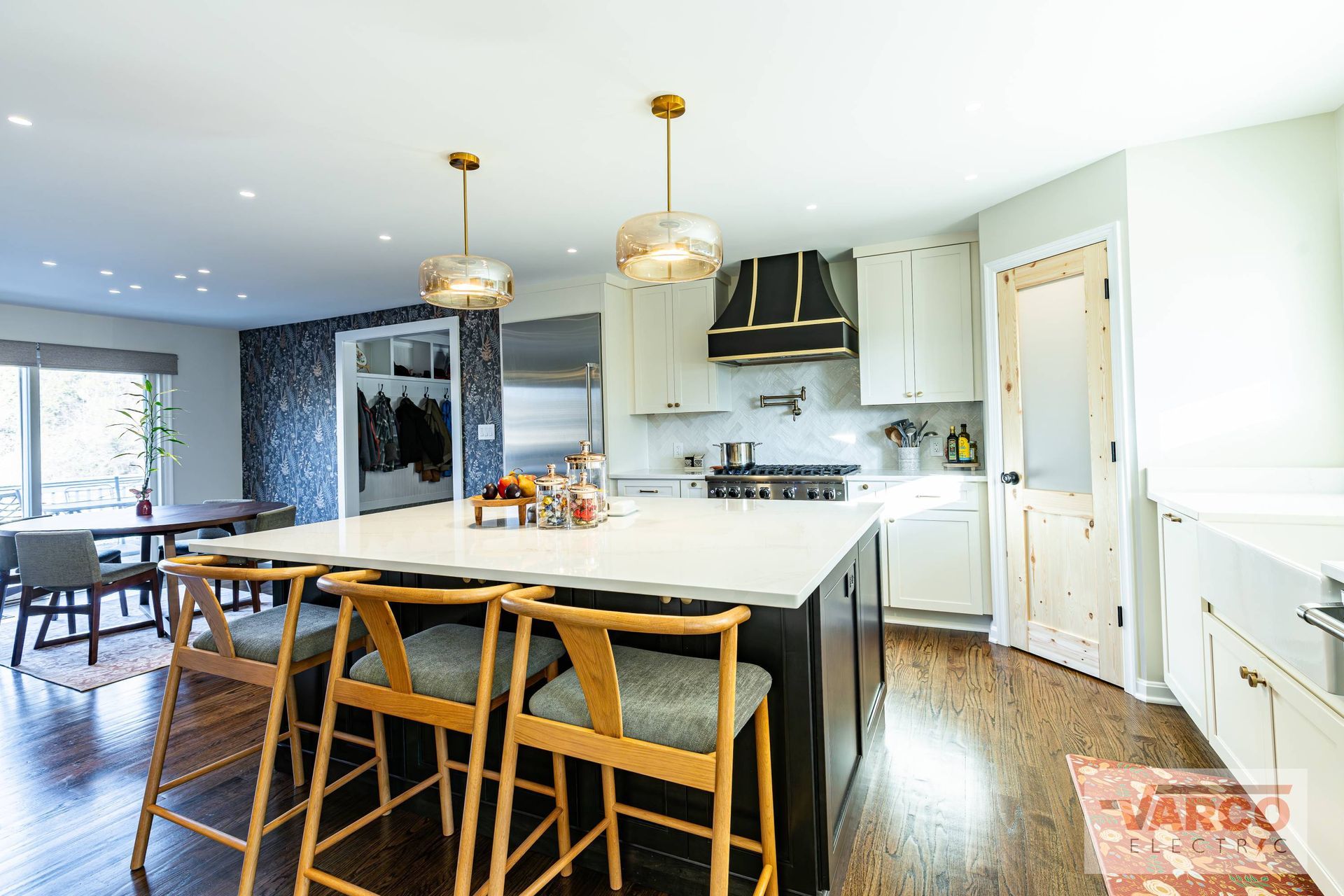 Spacious kitchen with island, seating, and gold pendant lights. Dark cabinets, white countertops, and wooden floors.