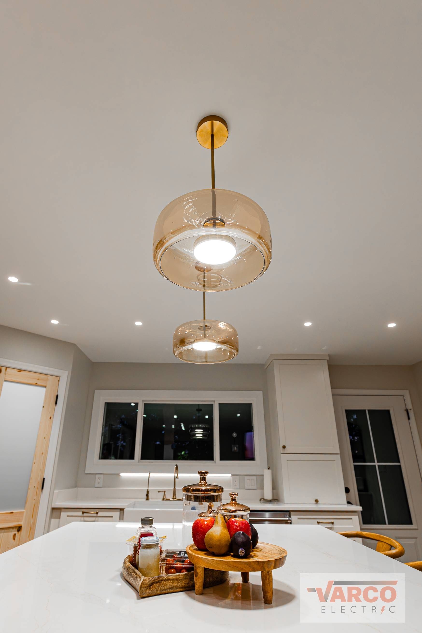 Three pendant lights illuminate a kitchen island with a decorative tray, cabinets, and a window in the background.