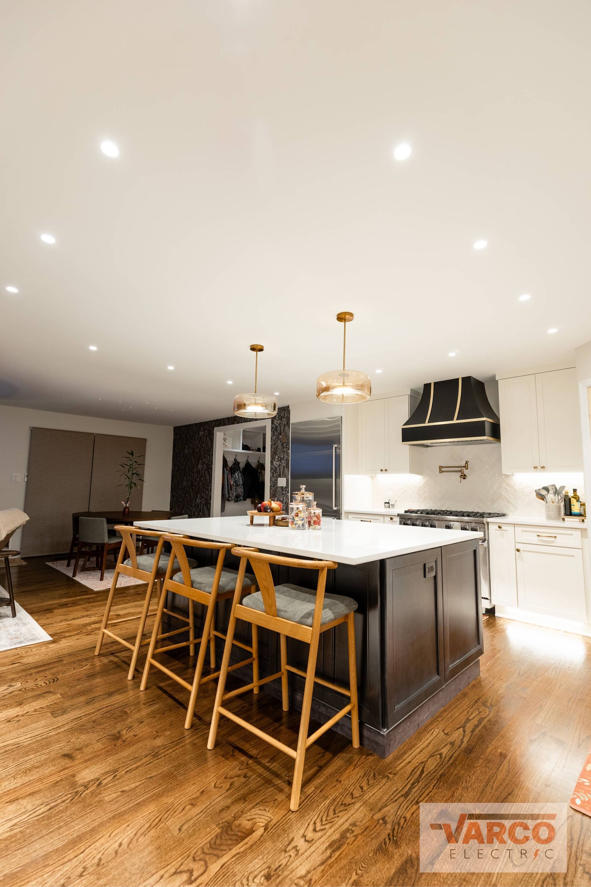 Modern kitchen with island, seating, dark cabinets, white countertops, and hardwood floor.