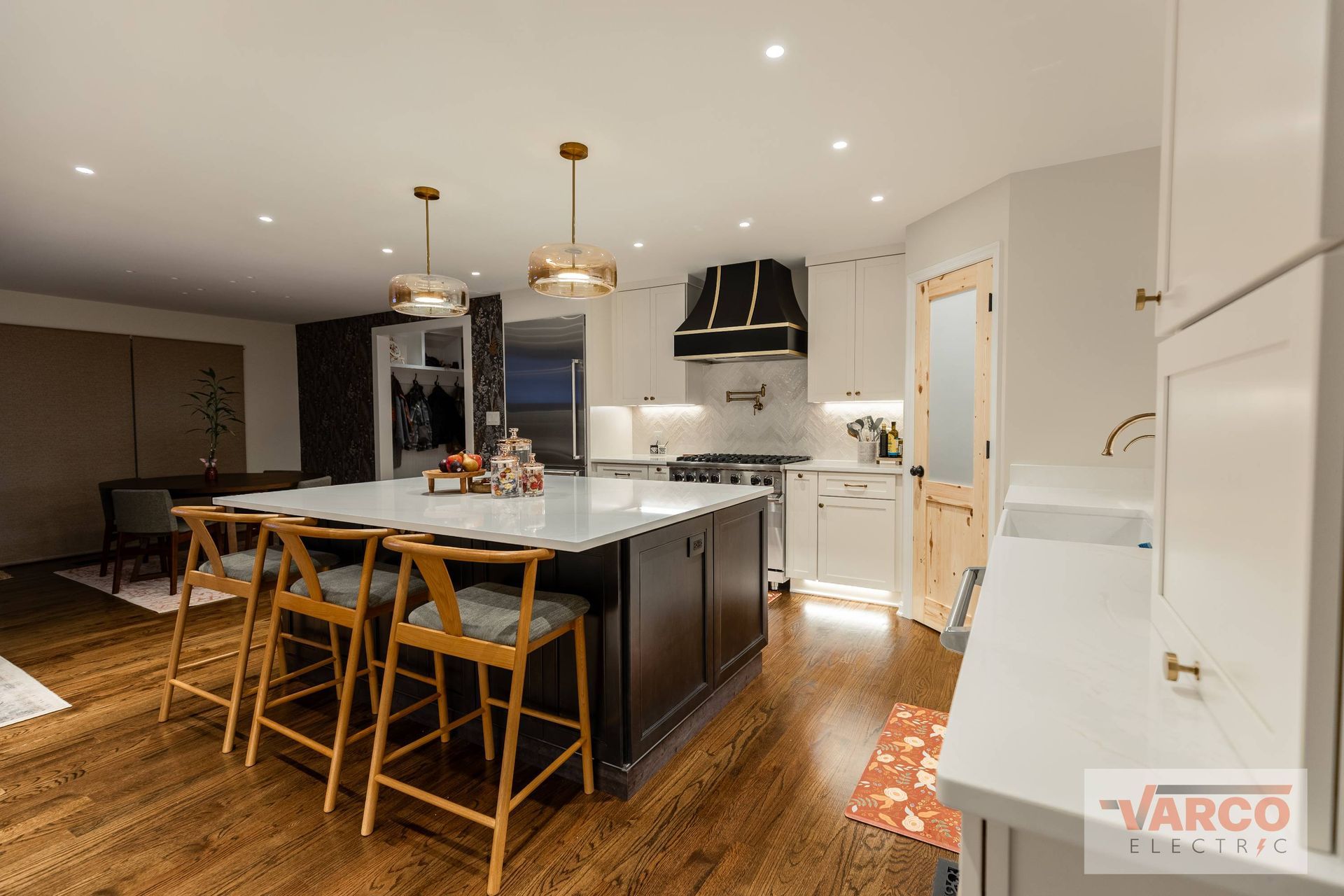 Modern kitchen with island, seating, marble countertops, pendant lights, dark cabinets, and wood flooring.